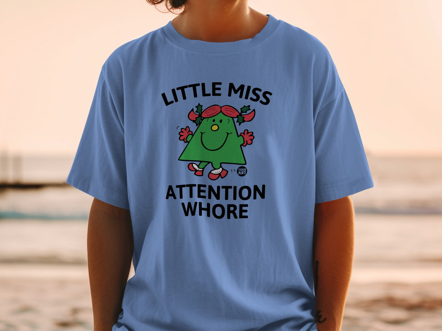 Blue t-shirt with "Little Miss Attention Whore" graphic of a smiling green Christmas tree.