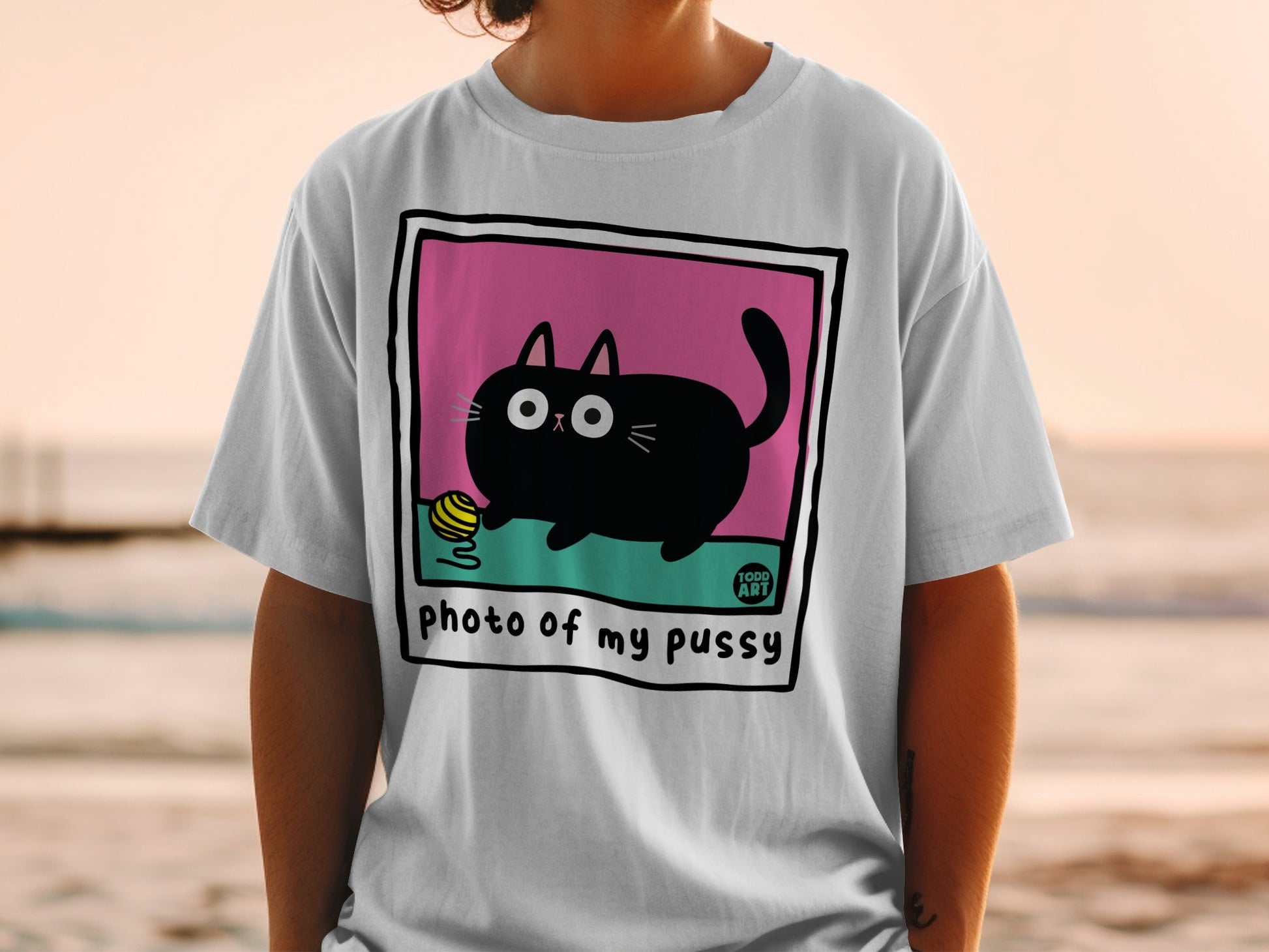White t-shirt featuring a cartoon black cat playing with a yellow ball of yarn.