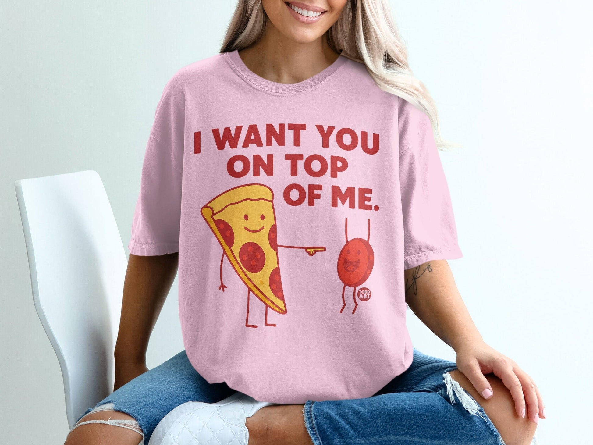 Pink t-shirt with cartoon pizza slice and pepperoni saying "I WANT YOU ON TOP OF ME."