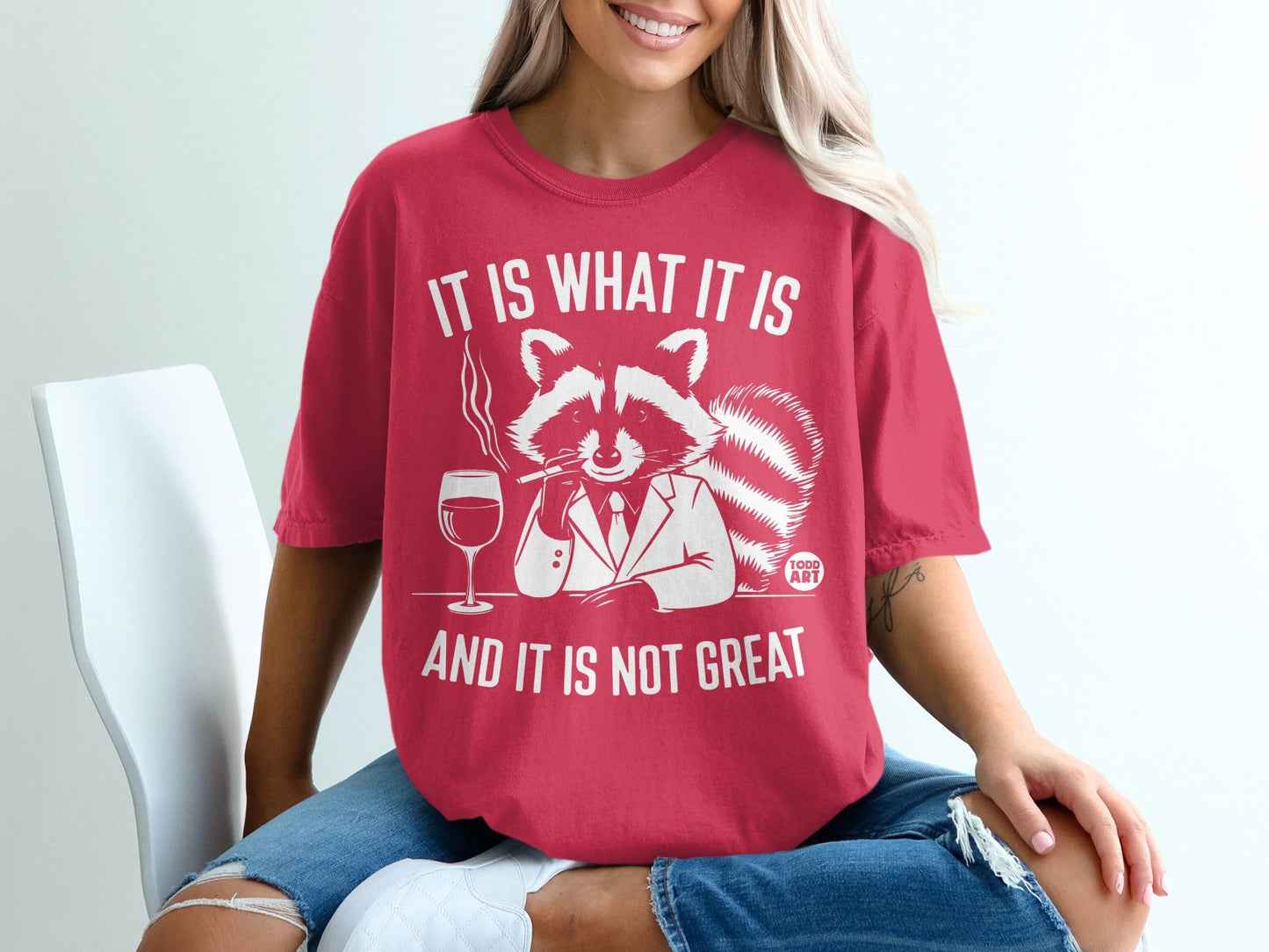 Red t-shirt with a raccoon in a suit smoking, holding wine, text says "IT IS WHAT IT IS AND IT IS NOT GREAT".