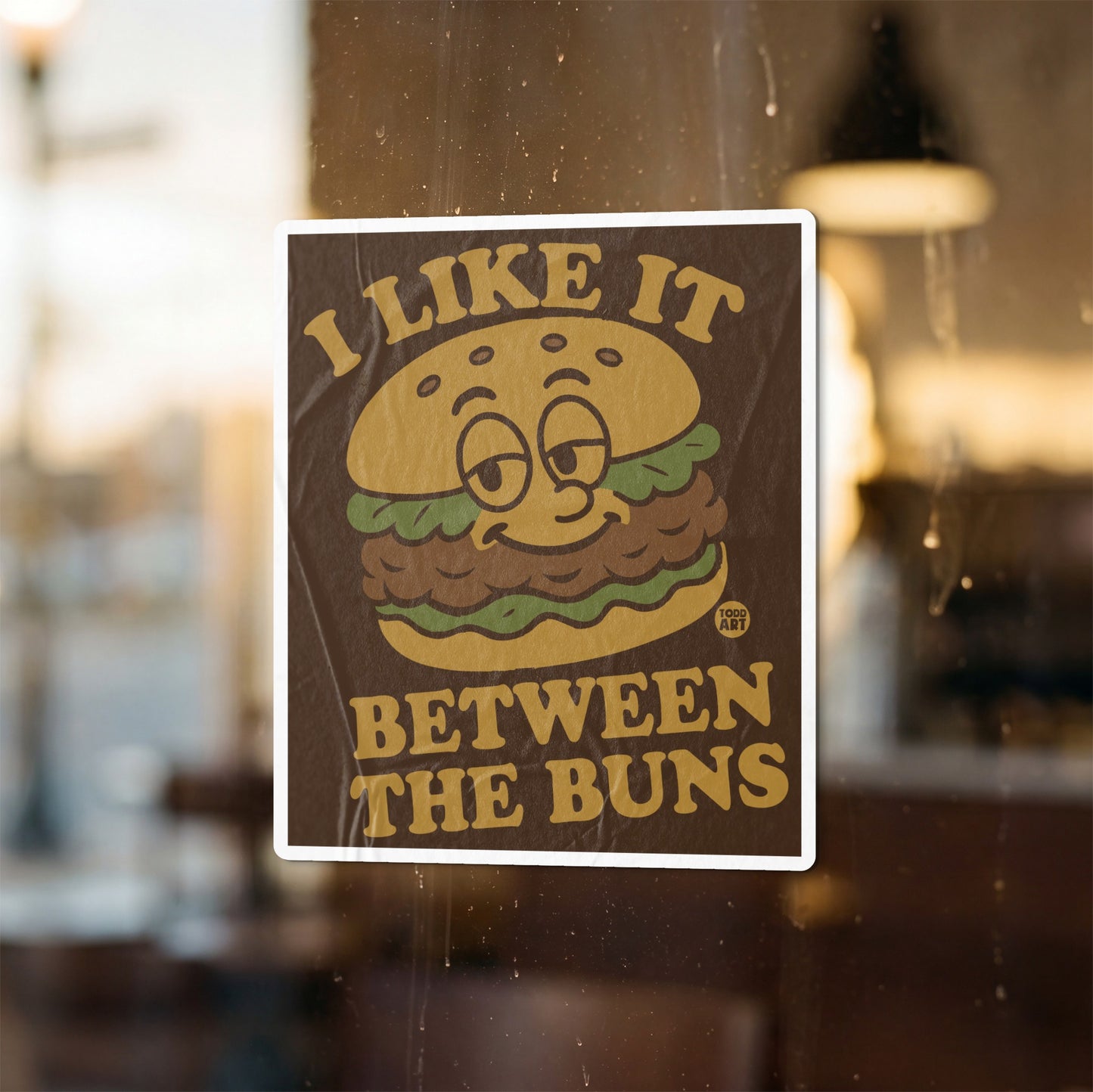 Brown sticker with a cartoon hamburger and text "I LIKE IT BETWEEN THE BUNS".