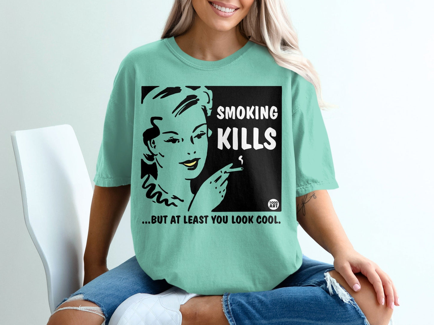 Teal t-shirt with black graphic: woman smoking, text "SMOKING KILLS...BUT AT LEAST YOU LOOK COOL".
