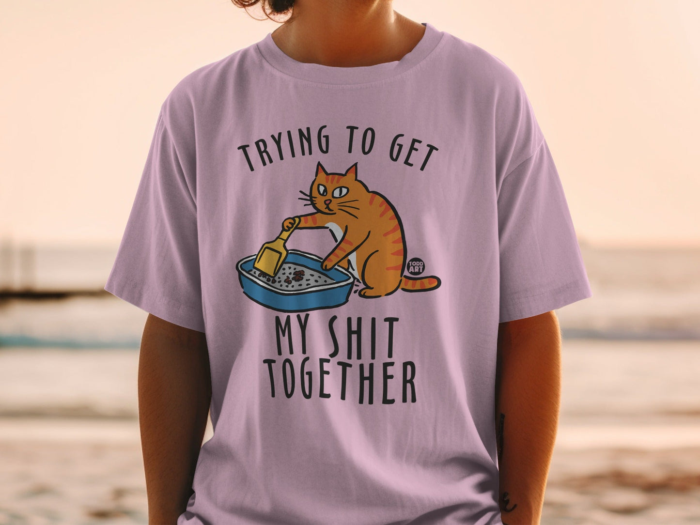Orange cat scooping litter box on purple t-shirt with text "Trying to get my shit together".