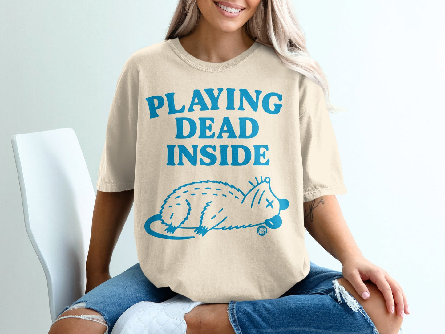 Cream t-shirt with blue text "PLAYING DEAD INSIDE" and a blue possum illustration.