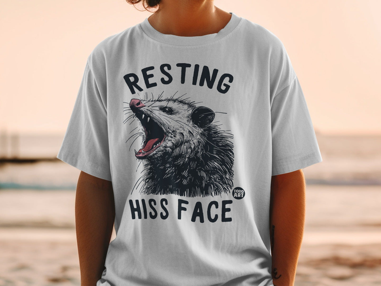 White t-shirt with a graphic of a hissing possum and text "RESTING HISS FACE".
