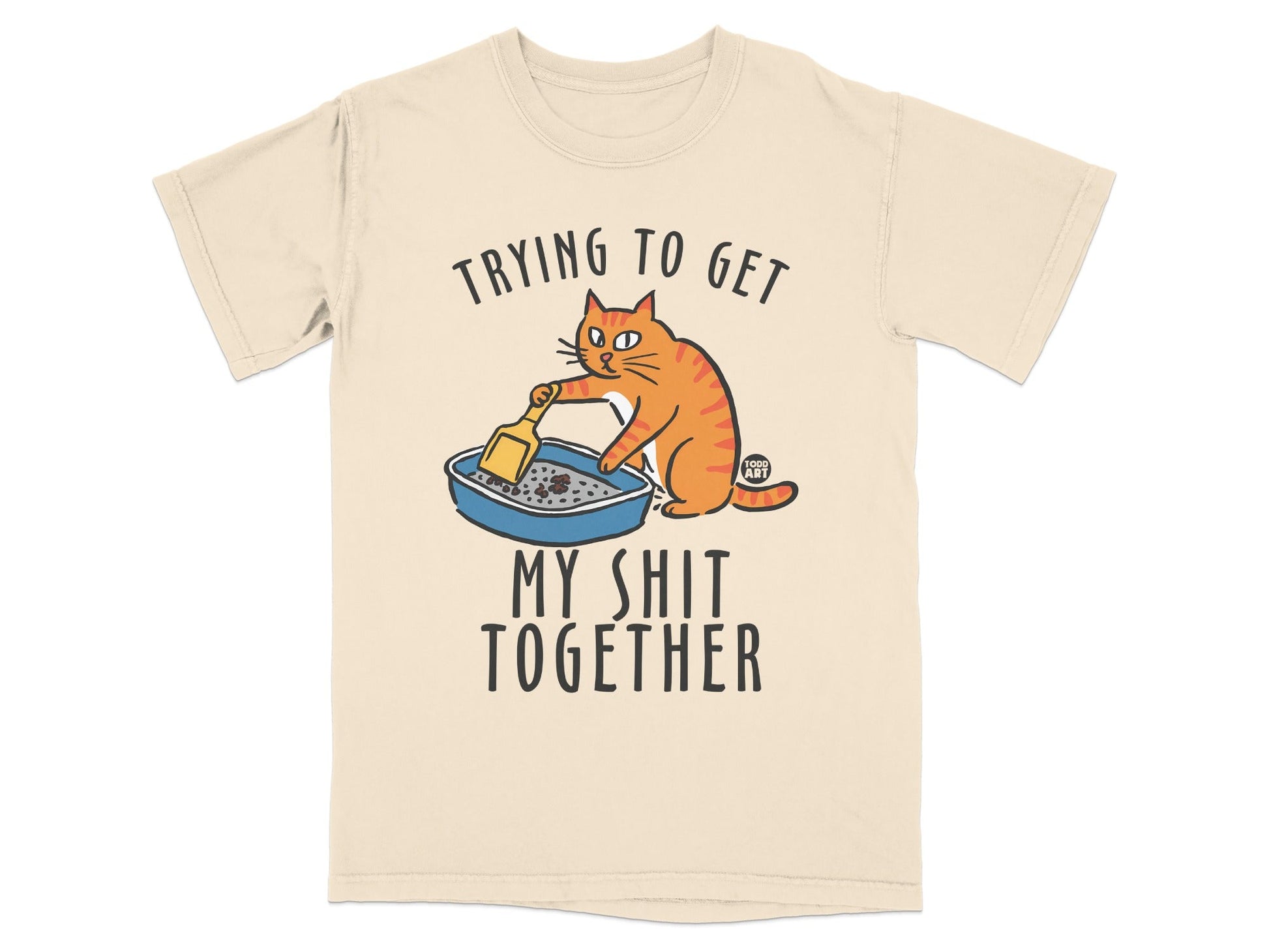 Cream t-shirt with cartoon cat cleaning litter box, text "Trying to Get My Shit Together".