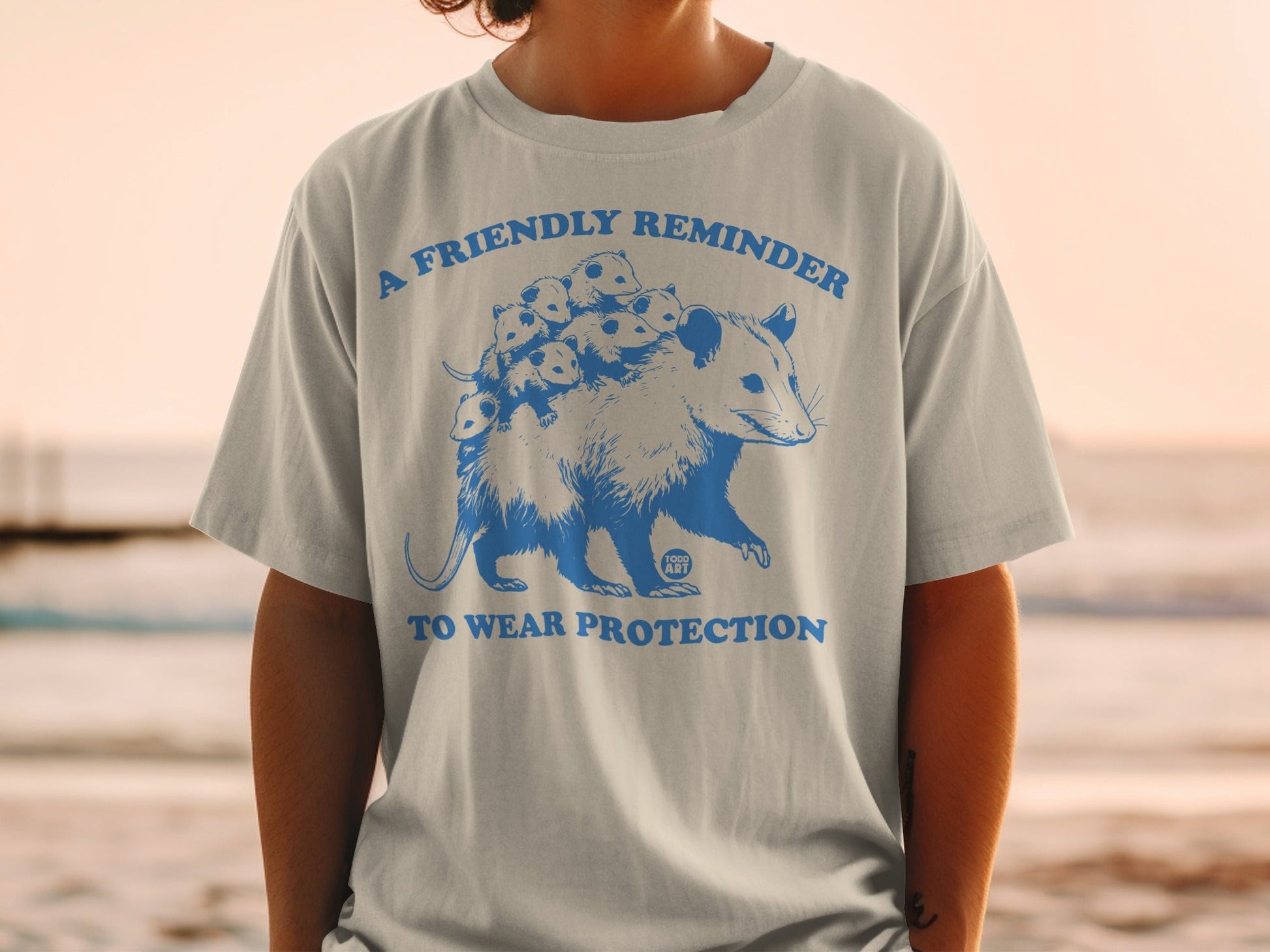 Grey t-shirt with a blue graphic of a possum carrying babies, saying "A Friendly Reminder To Wear Protection".