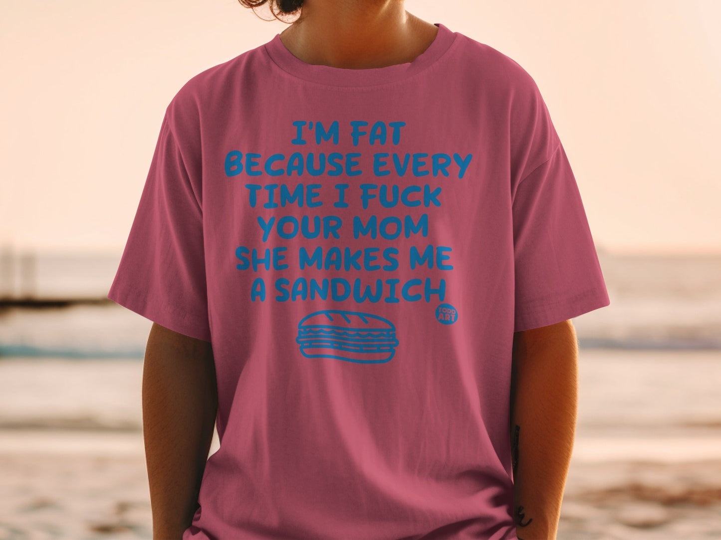 Pink t-shirt with blue text: "I'M FAT BECAUSE EVERY TIME I FUCK YOUR MOM SHE MAKES ME A SANDWICH", with a sandwich illustration.