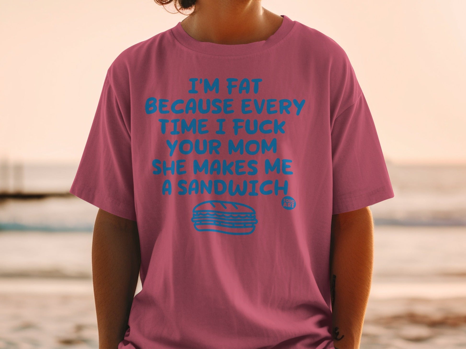 Pink t-shirt with blue text: "I'M FAT BECAUSE EVERY TIME I FUCK YOUR MOM SHE MAKES ME A SANDWICH", with a sandwich illustration.