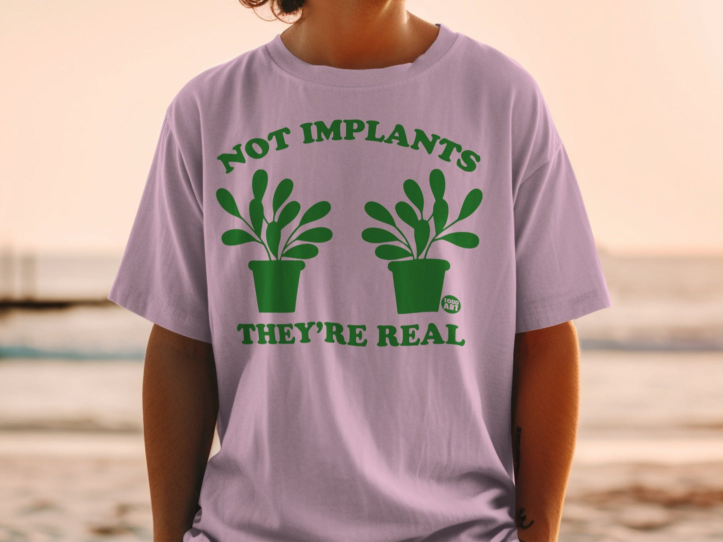 T-shirt with green text "NOT IMPLANTS THEY'RE REAL" and two potted plants.