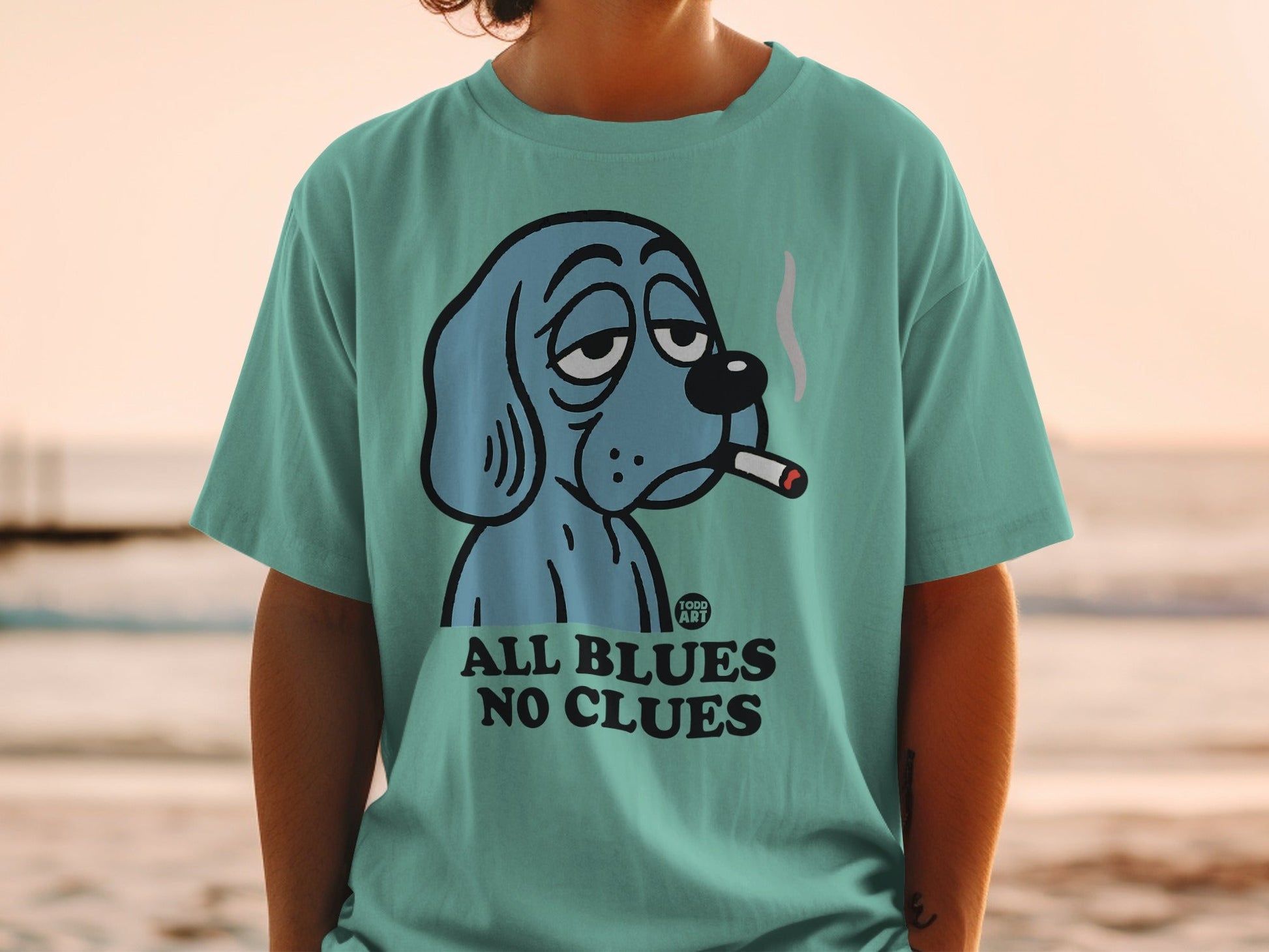 Teal t-shirt with cartoon dog smoking cigarette and text "ALL BLUES NO CLUES".