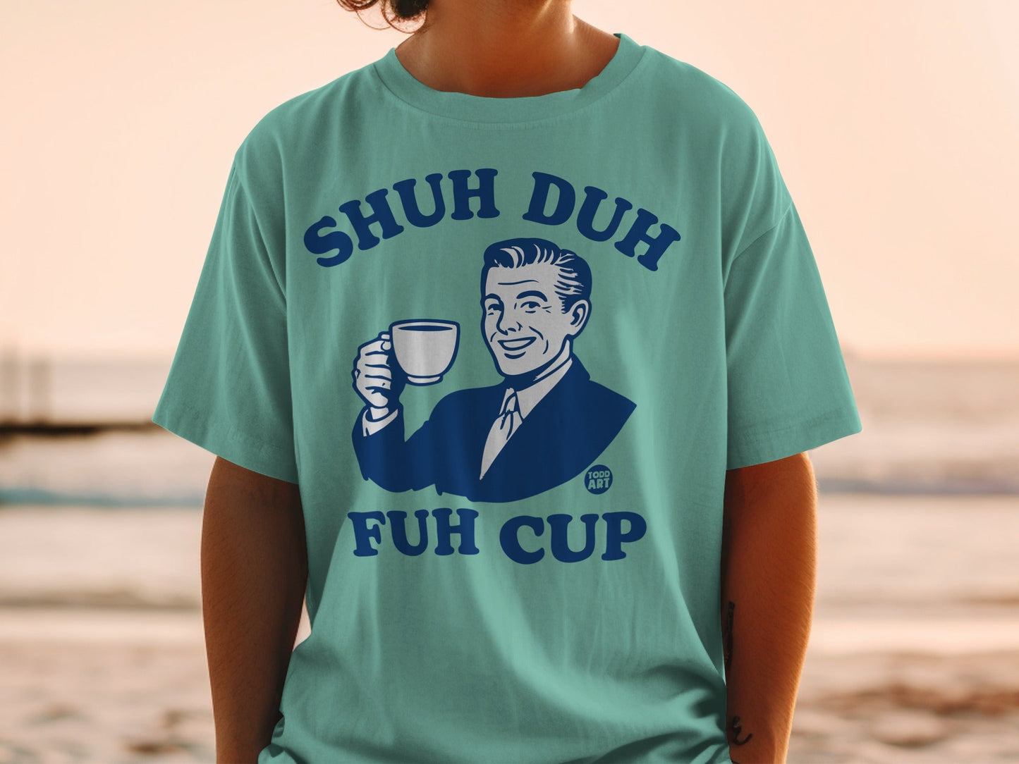 Teal t-shirt with graphic of man holding coffee mug, "SHUH DUH FUH CUP" text.