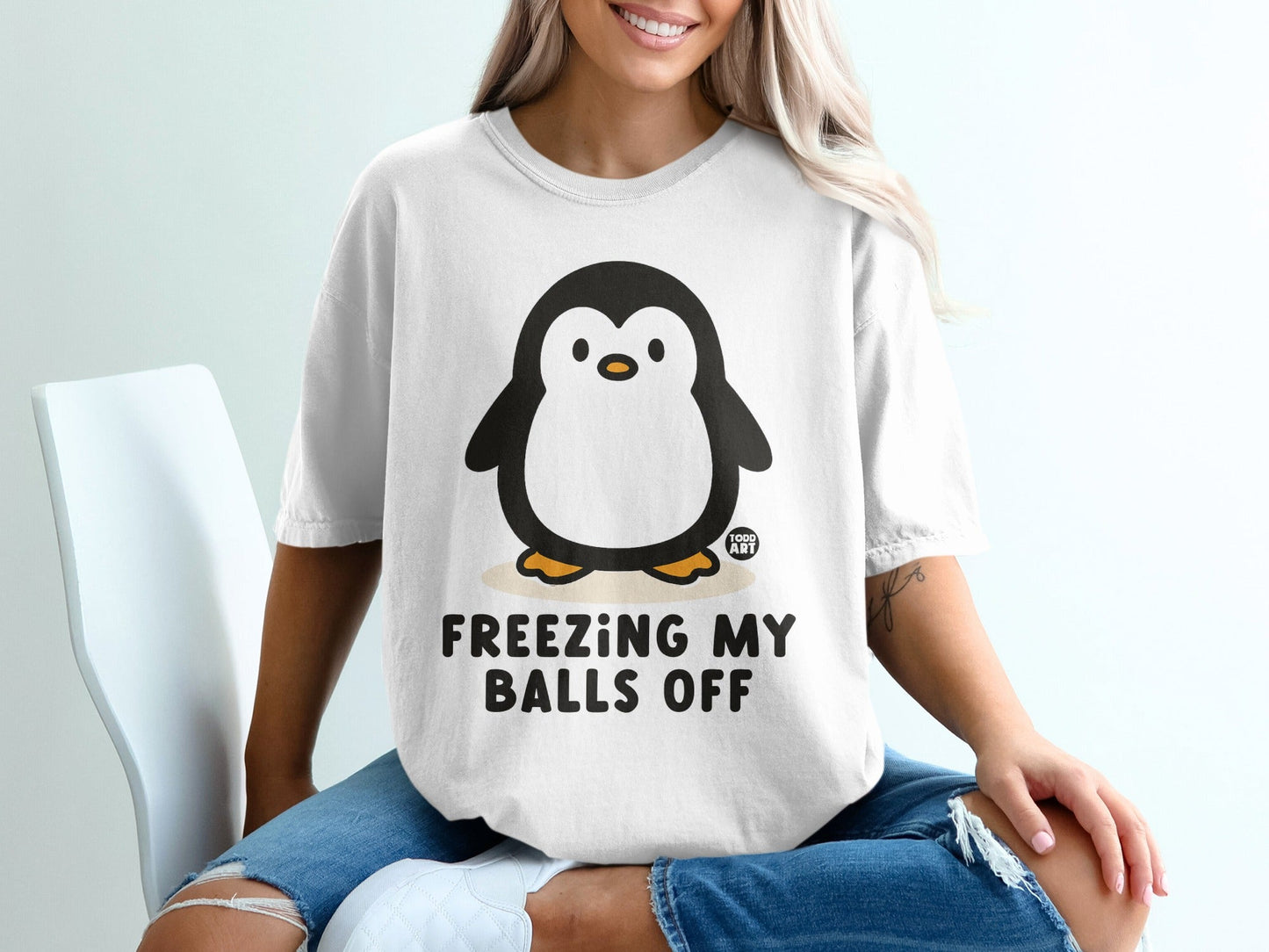 White t-shirt with cartoon penguin and text "FREEZING MY BALLS OFF".
