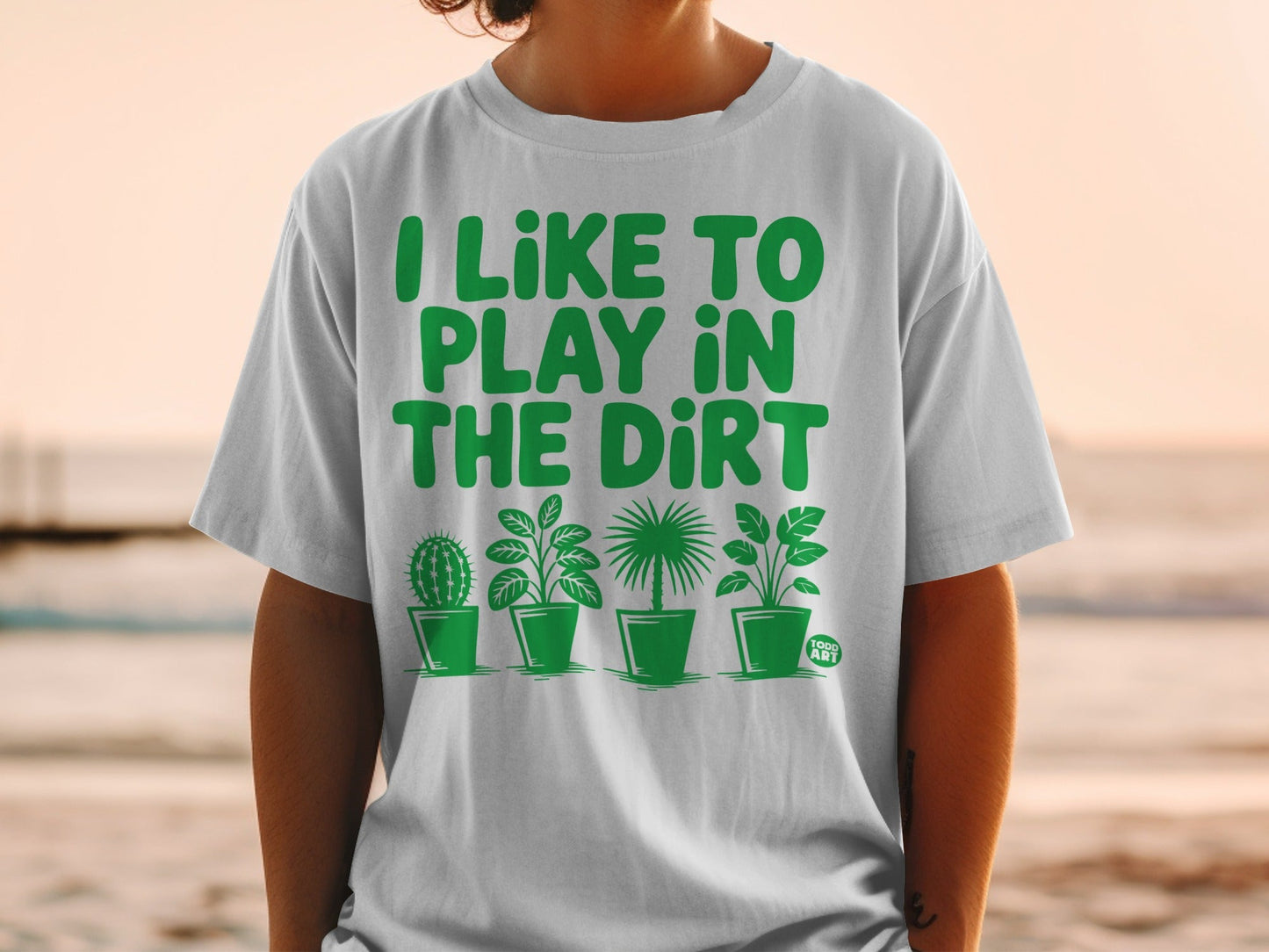 White t-shirt with green text "I LIKE TO PLAY IN THE DIRT" and four potted plants.