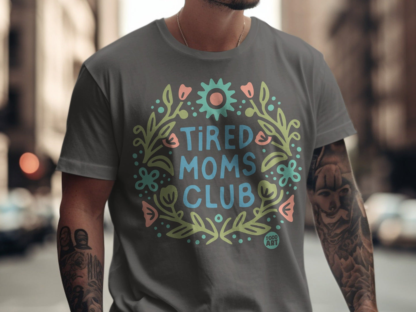 Grey t-shirt with "TIRED MOMS CLUB" text in floral wreath design.