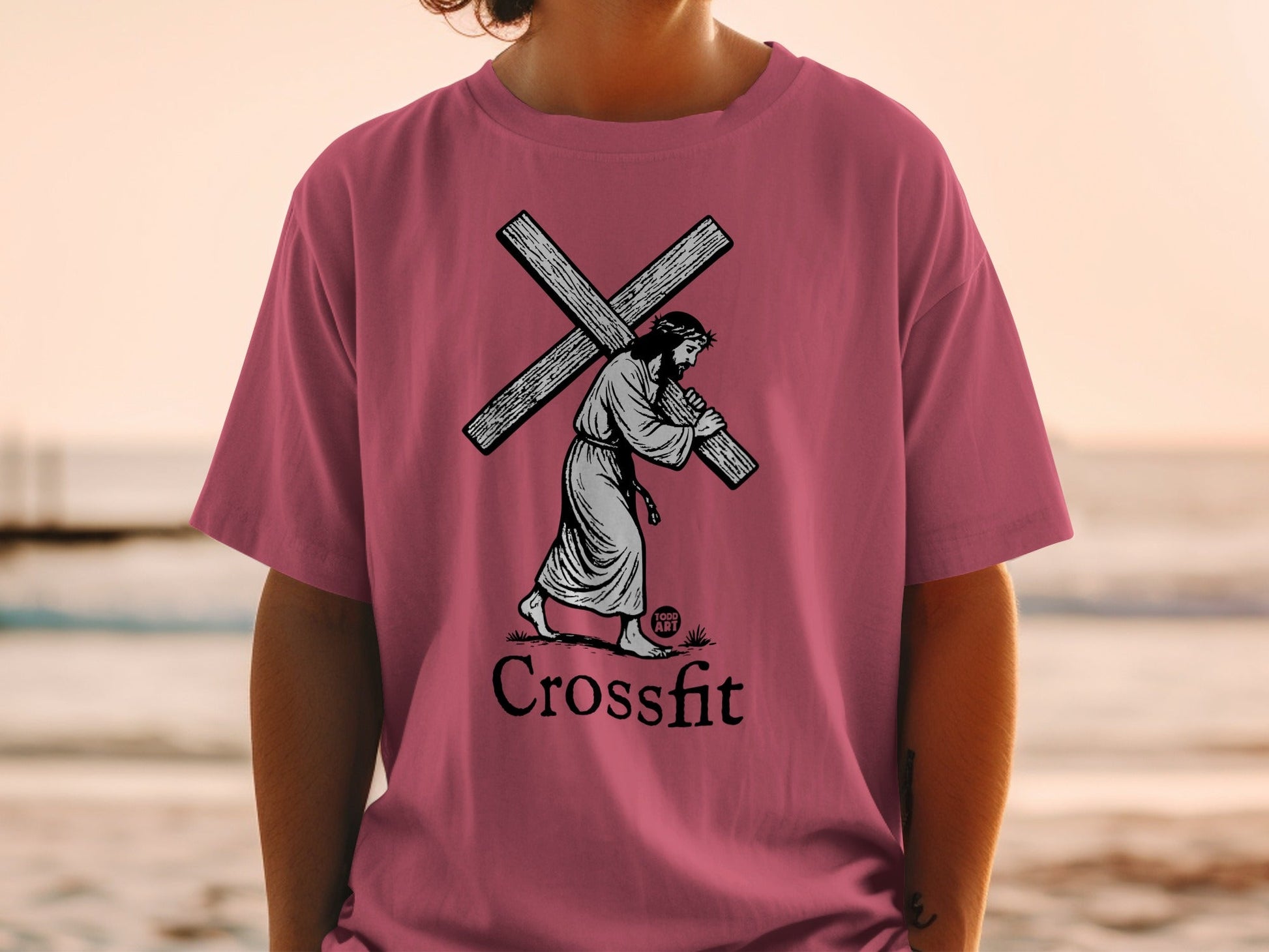 Jesus carrying a cross on a dark pink t-shirt, with "CrossFit" below.