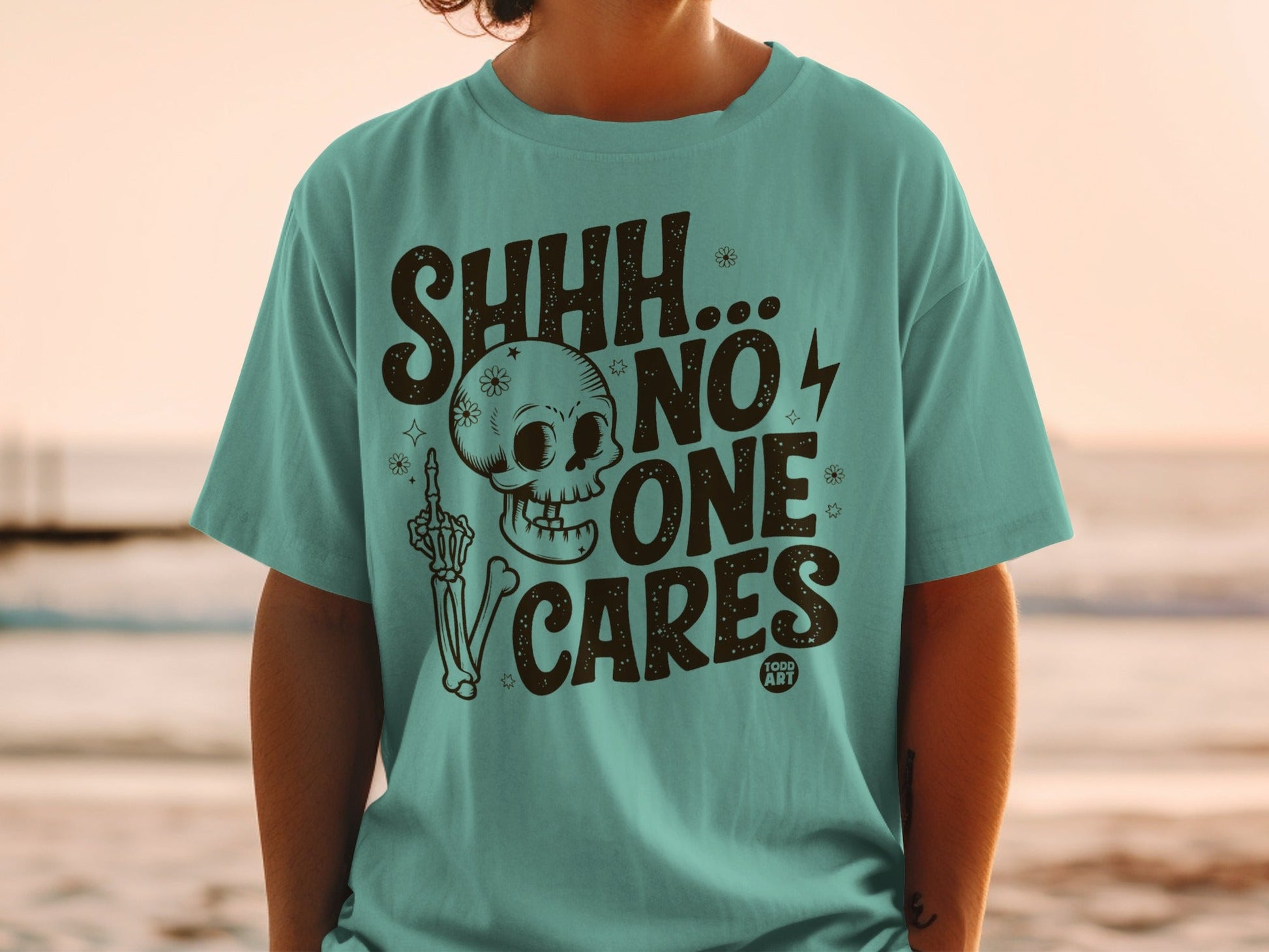 Teal t-shirt with skull, skeleton hand, and "SHHH... NO ONE CARES" text.