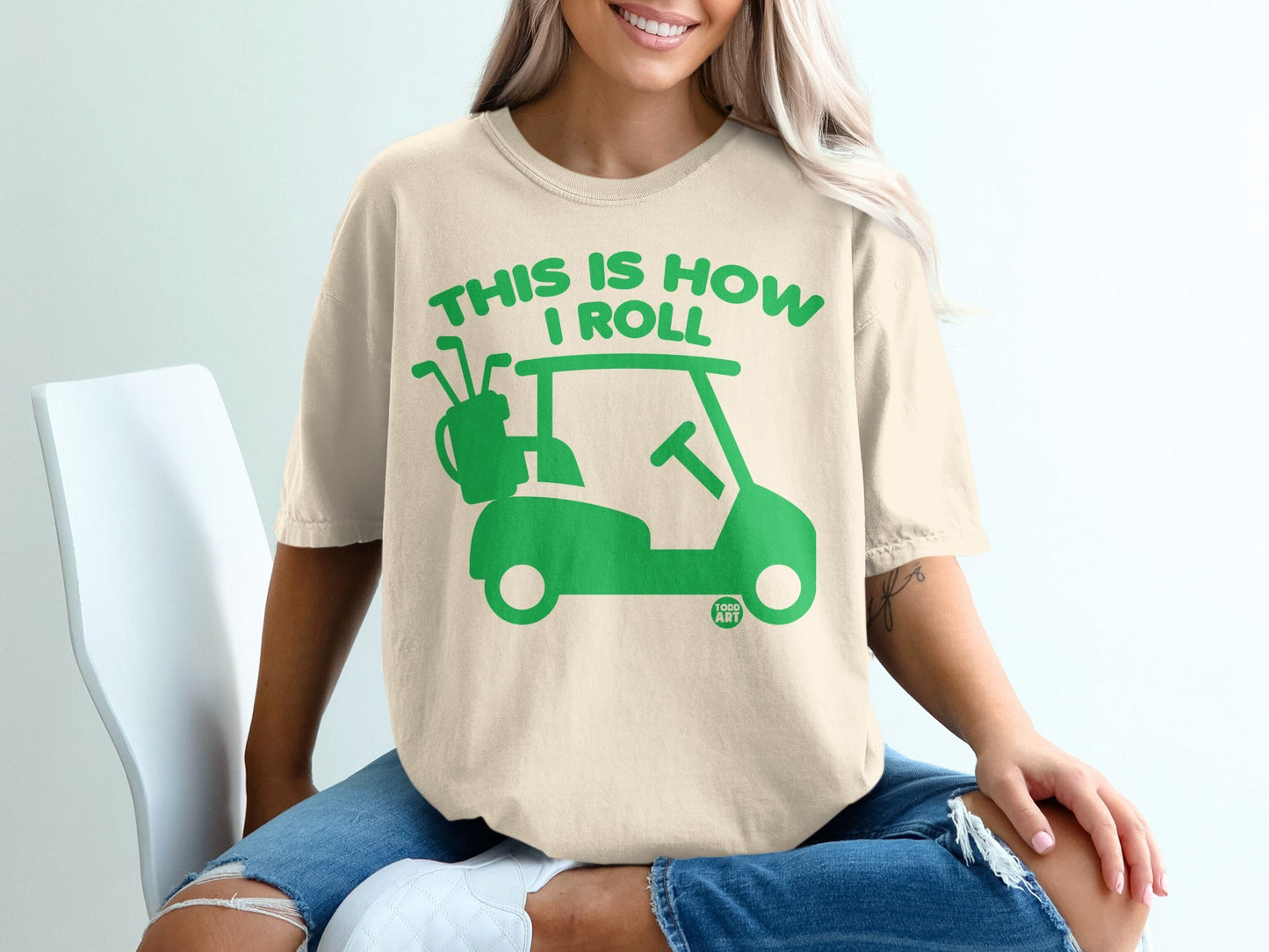 Cream t-shirt with green golf cart graphic and "THIS IS HOW I ROLL" text.