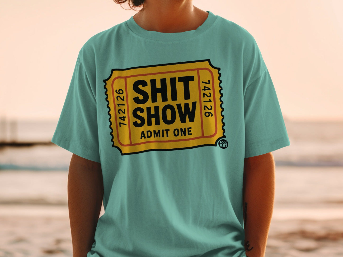 Teal t-shirt with "SHIT SHOW ADMIT ONE" printed in a yellow ticket design.