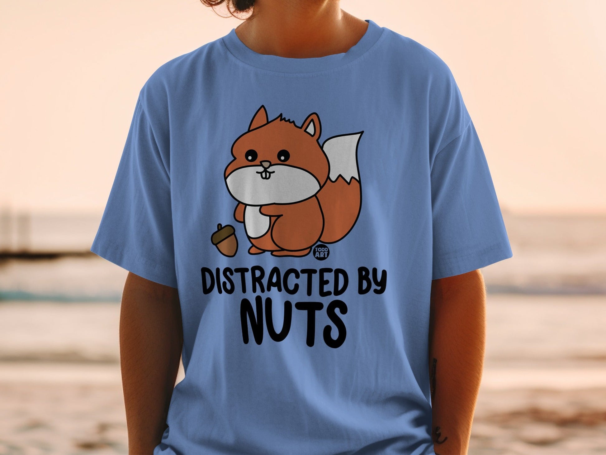 Blue t-shirt with cartoon squirrel holding an acorn and text "DISTRACTED BY NUTS".