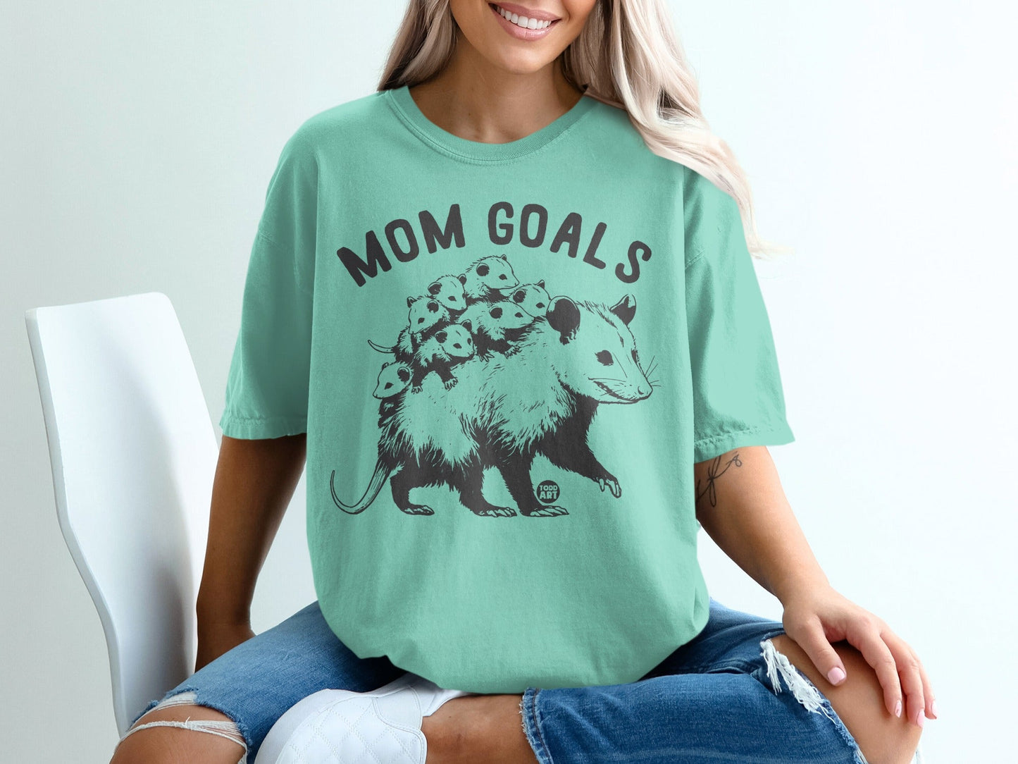 Opossum mom and babies graphic with "MOM GOALS" text on a teal t-shirt.