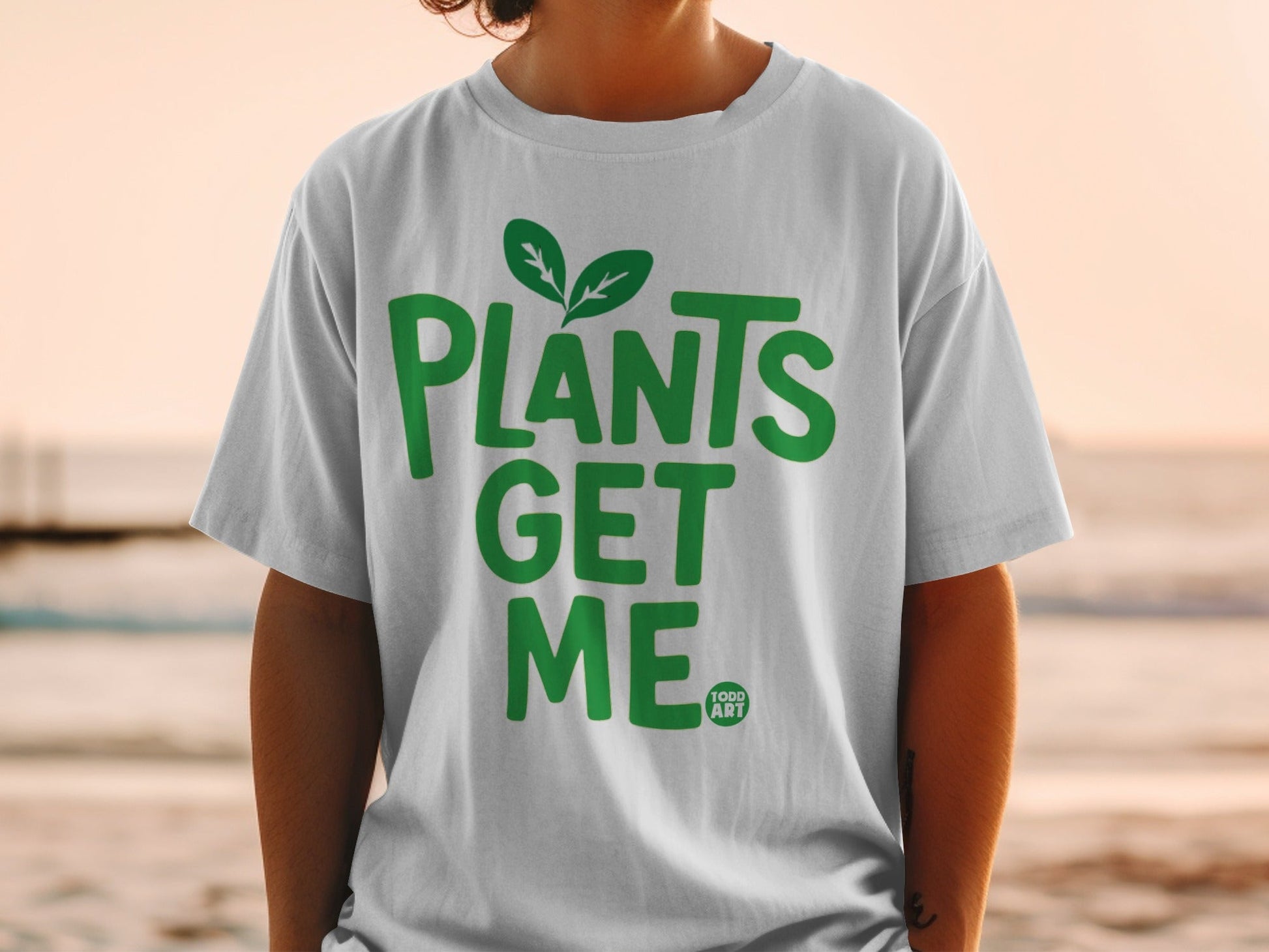 White t-shirt with green text "PLANTS GET ME" and small leaf graphic.