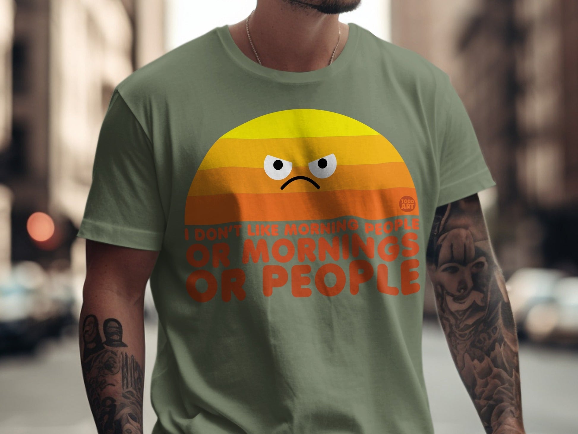 Green t-shirt with orange graphic of a grumpy sun and text "I DON'T LIKE MORNING PEOPLE OR PEOPLE".