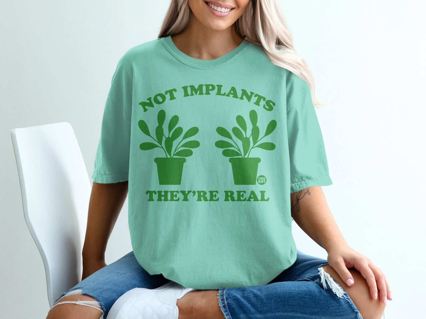Mint green t-shirt with "Not implants, they're real" and plant graphic.
