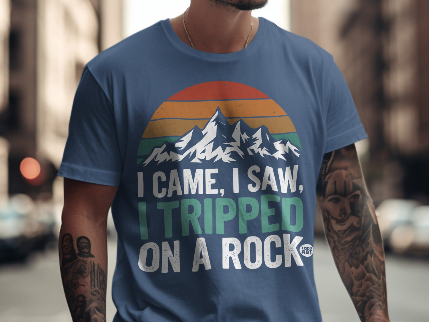 Blue t-shirt with "I CAME, I SAW, I TRIPPED ON A ROCK" and mountain graphic.