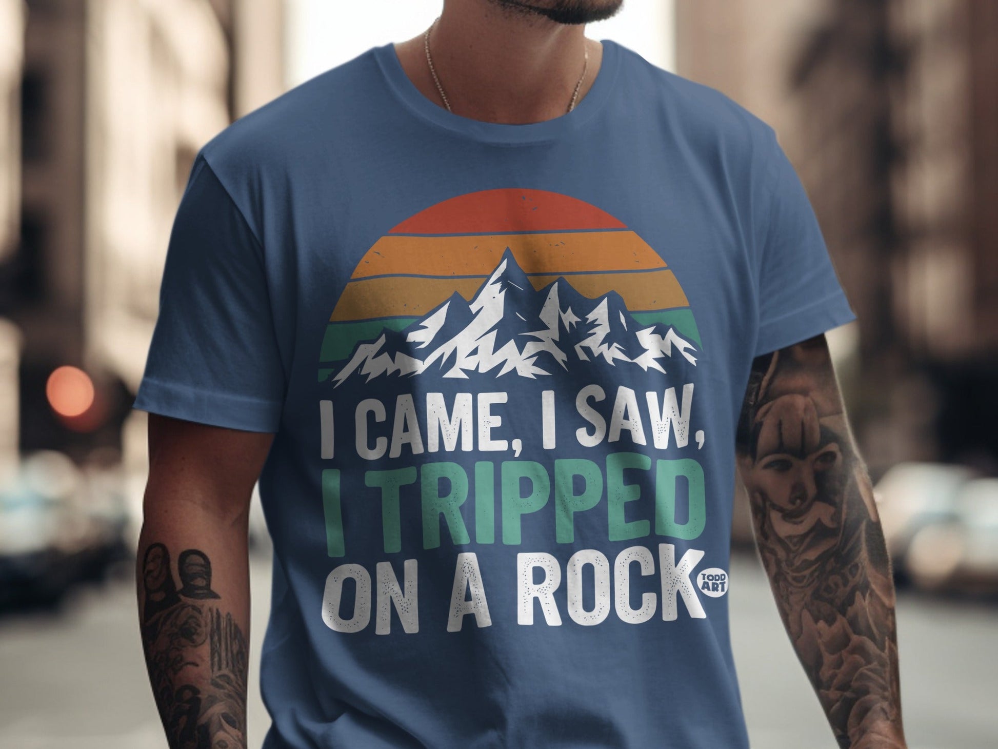 Blue t-shirt with "I CAME, I SAW, I TRIPPED ON A ROCK" and mountain graphic.
