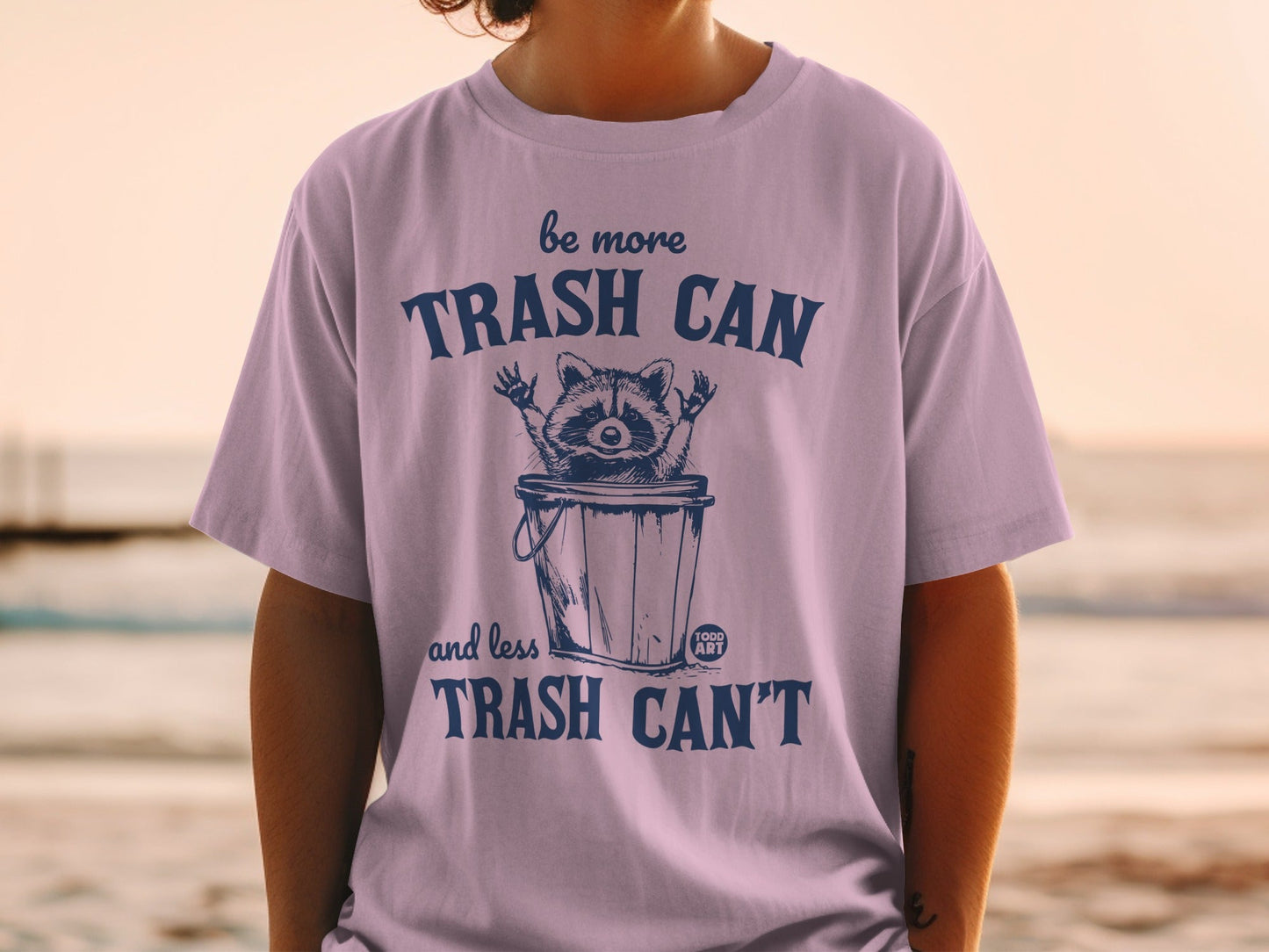 T-shirt with raccoon in trash can and text "be more TRASH CAN and less TRASH CAN'T".