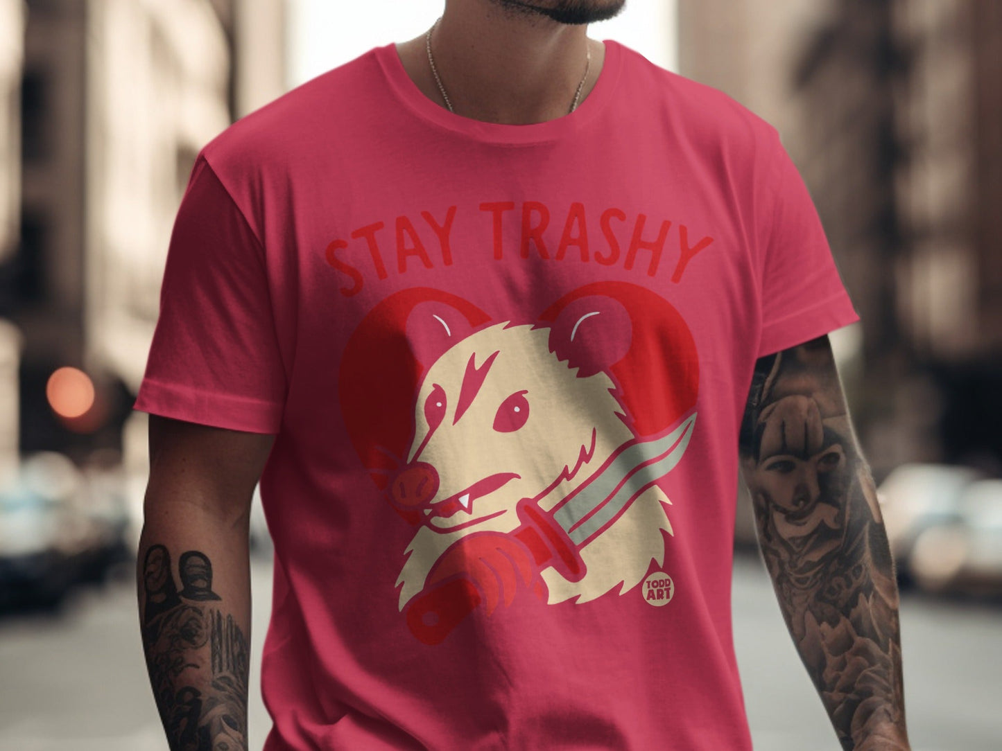 Pink t-shirt with "STAY TRASHY" and a possum holding a knife.