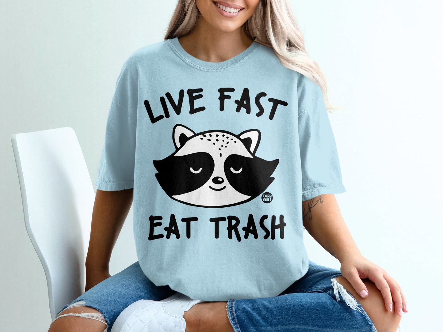 Light blue t-shirt with raccoon graphic and text "LIVE FAST EAT TRASH".