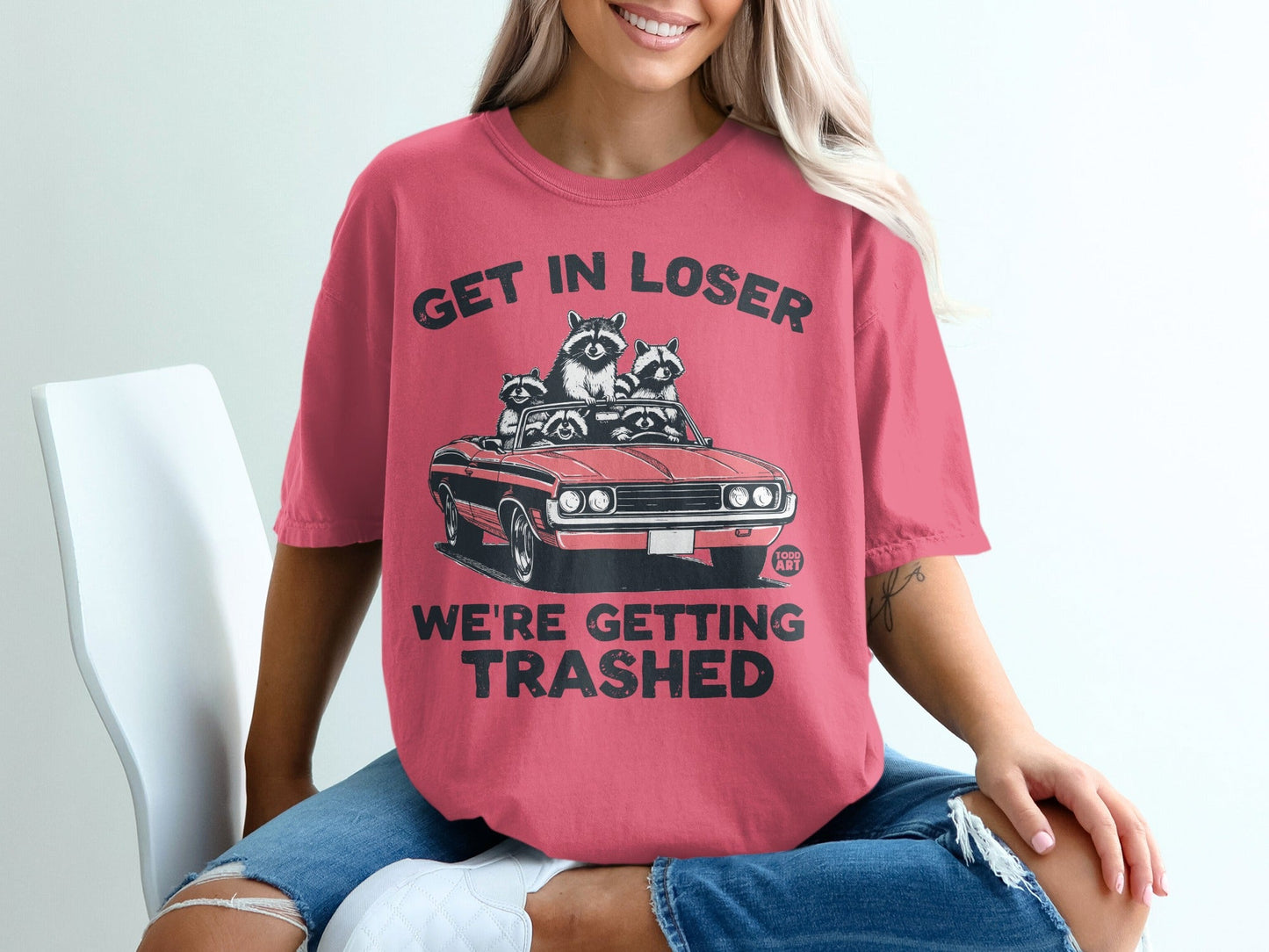 Pink t-shirt with graphic of raccoons in a convertible, text "GET IN LOSER WE'RE GETTING TRASHED".
