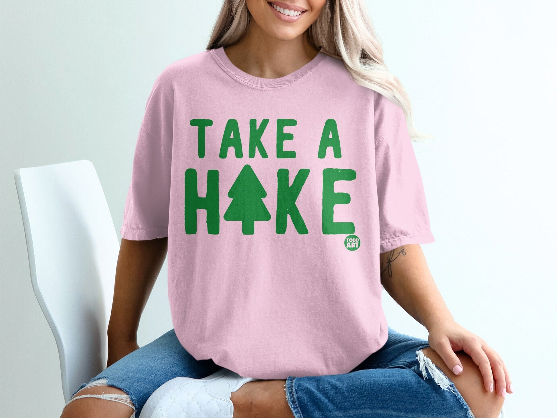 Pink t-shirt with green "TAKE A HIKE" text and a pine tree graphic.