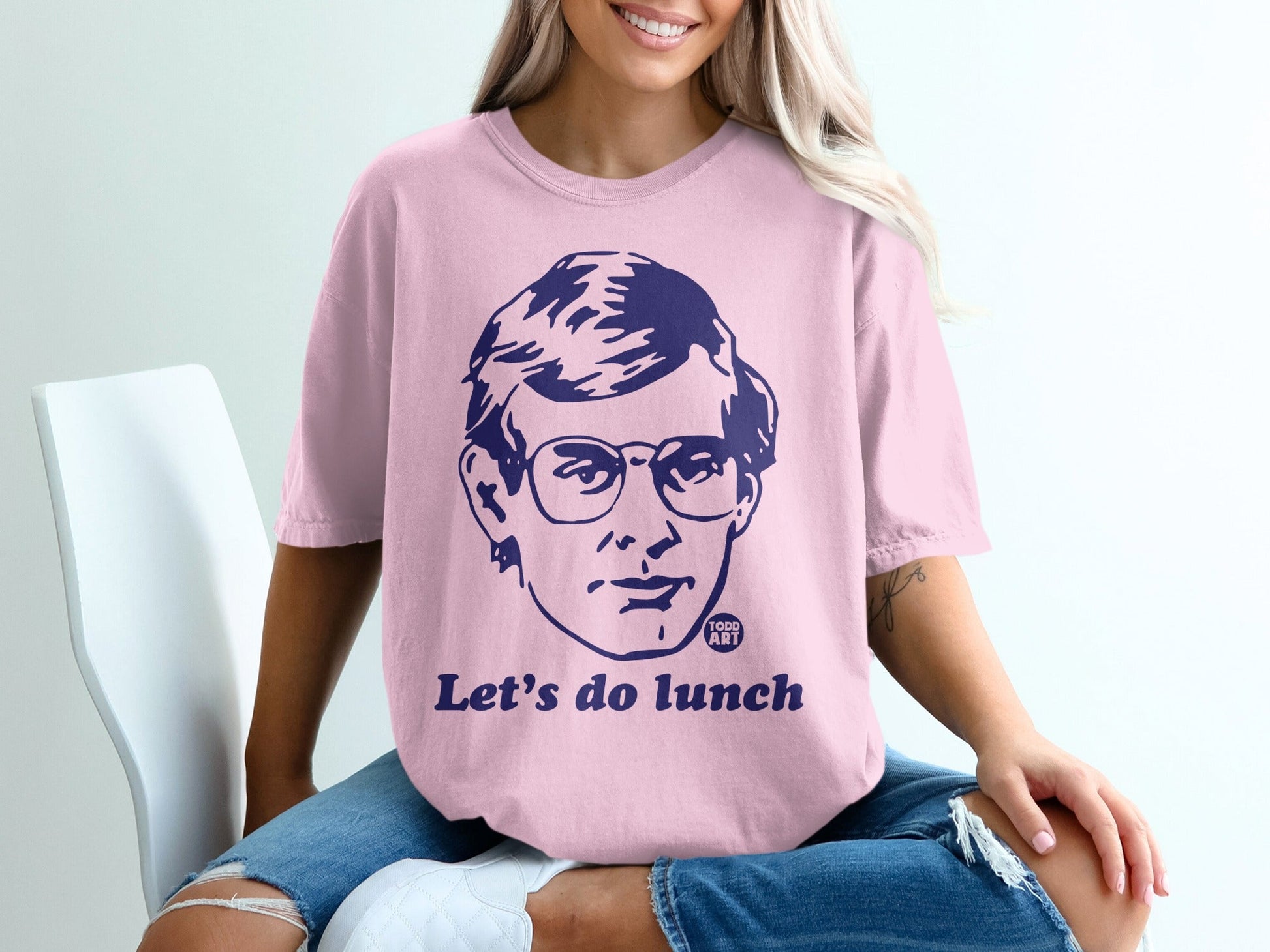 Pink t-shirt with a navy blue graphic of a man's face and the text "Let's do lunch".