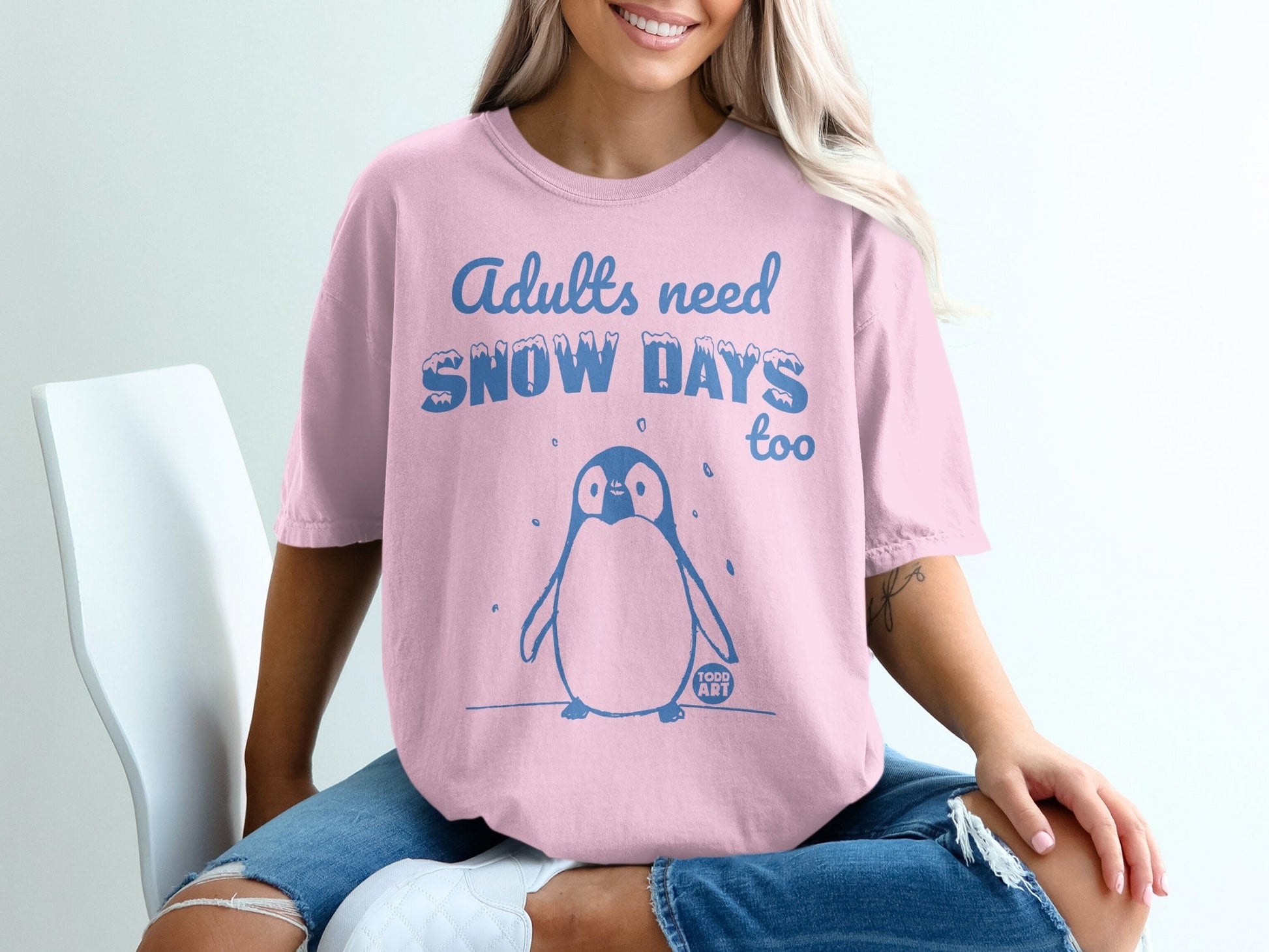 Pink t-shirt with blue text "Adults need snow days too" and cartoon penguin.