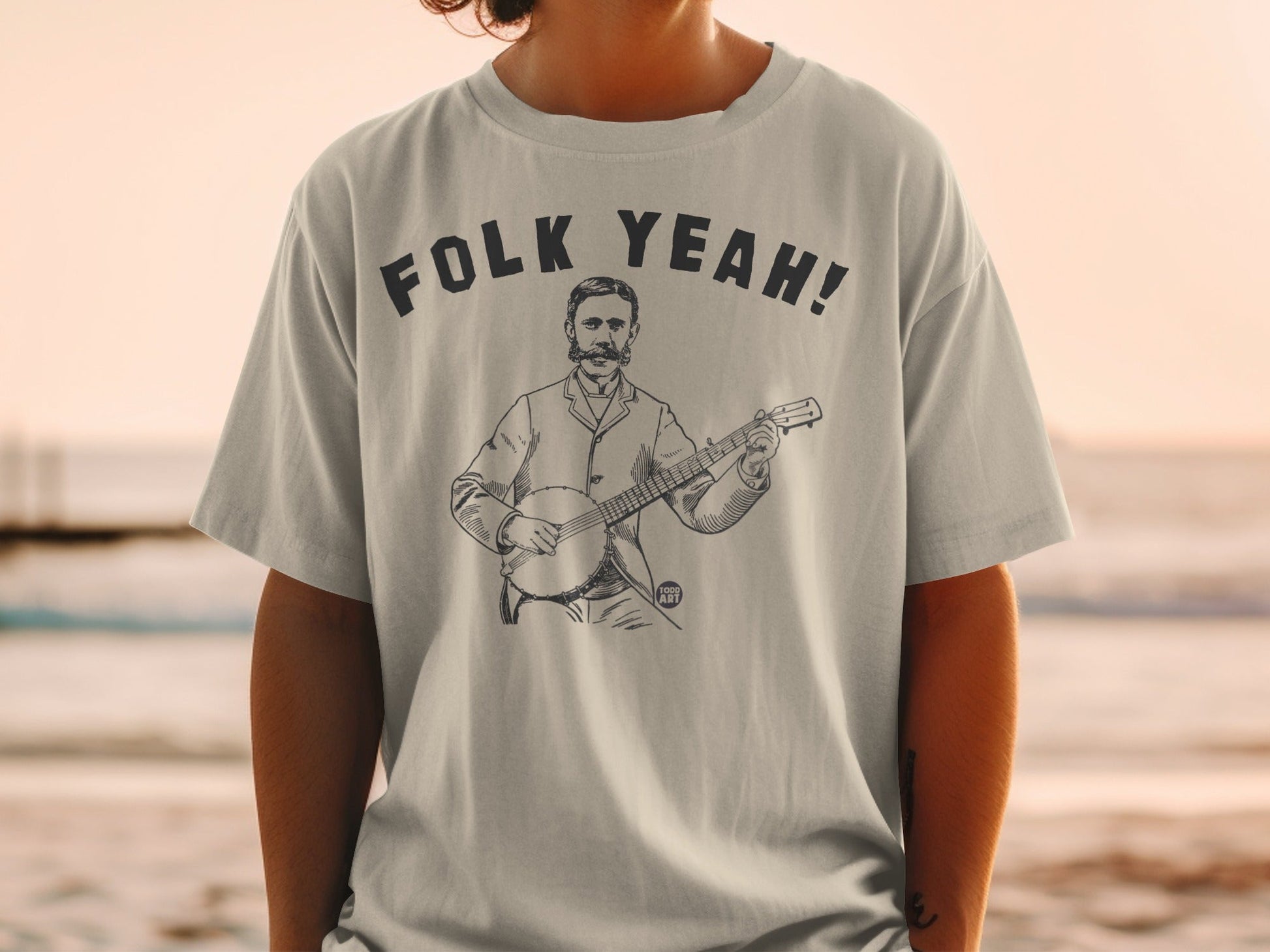 Light gray t-shirt with "FOLK YEAH!" text and drawing of a man playing a banjo.