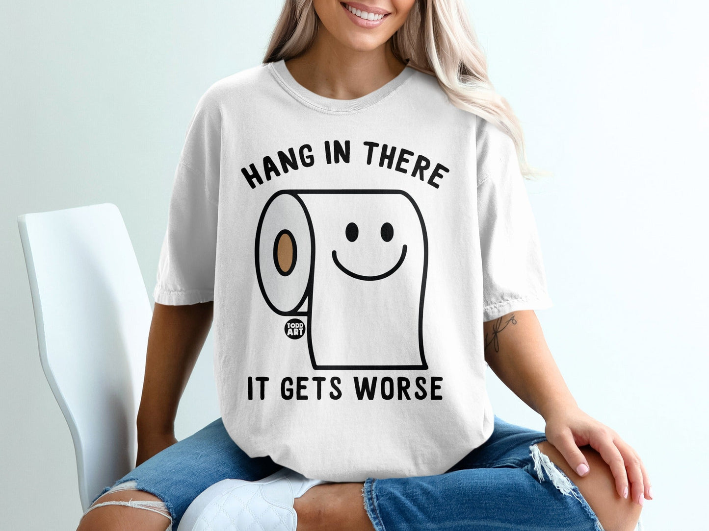 White t-shirt with "Hang in there it gets worse" and a smiling toilet paper roll.