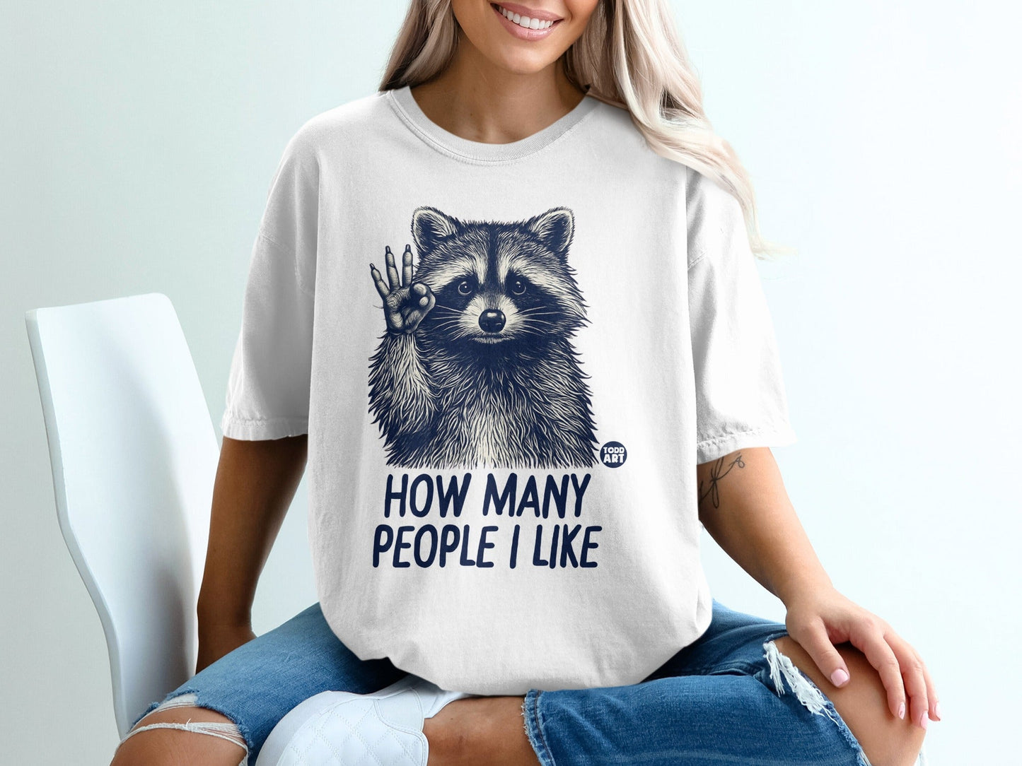 T-shirt with raccoon graphic and text "HOW MANY PEOPLE I LIKE".
