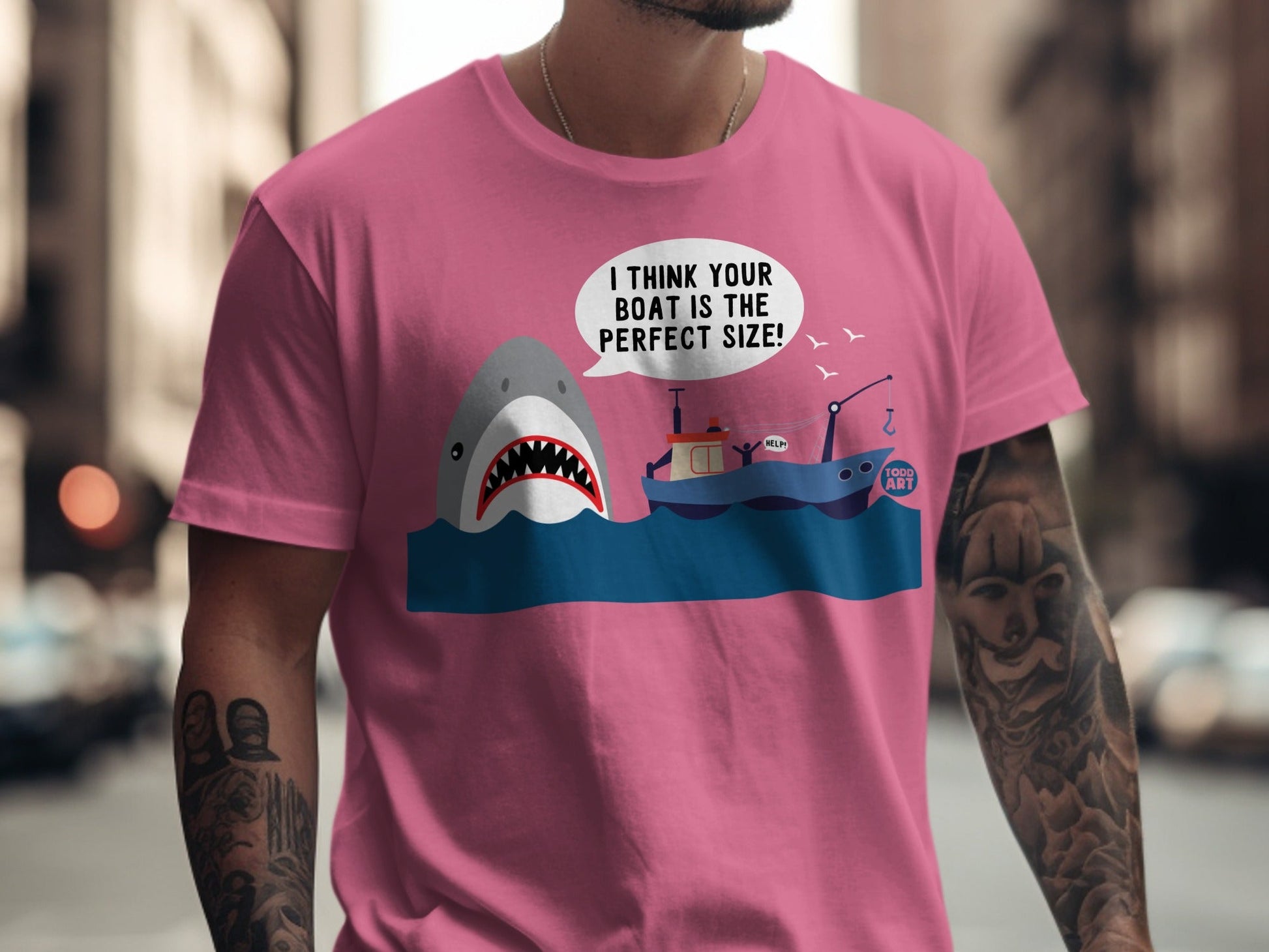 Pink t-shirt with shark and boat graphic, text reads "I THINK YOUR BOAT IS THE PERFECT SIZE!"