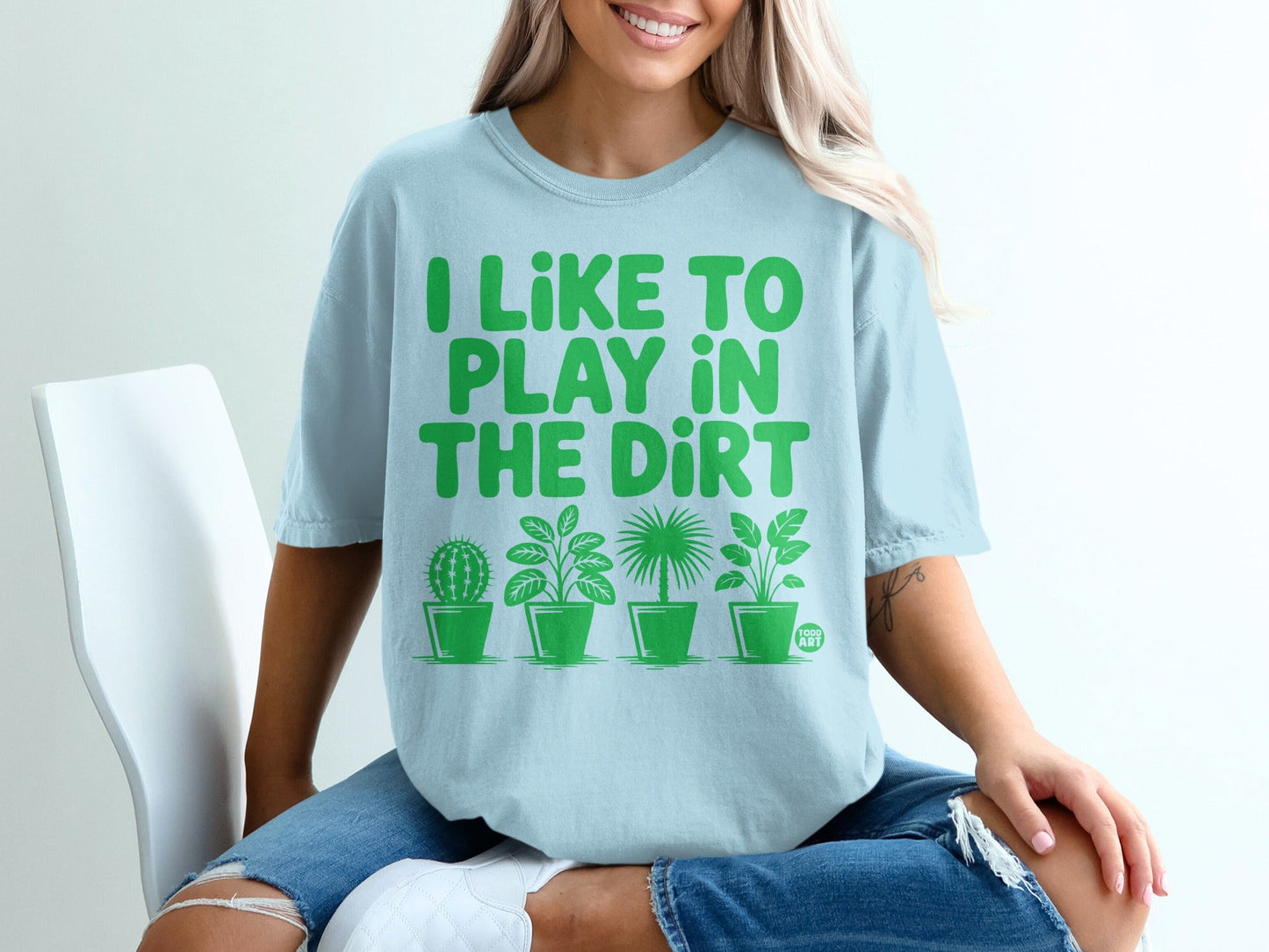 Light blue t-shirt with green text "I LIKE TO PLAY IN THE DIRT" and potted plants.