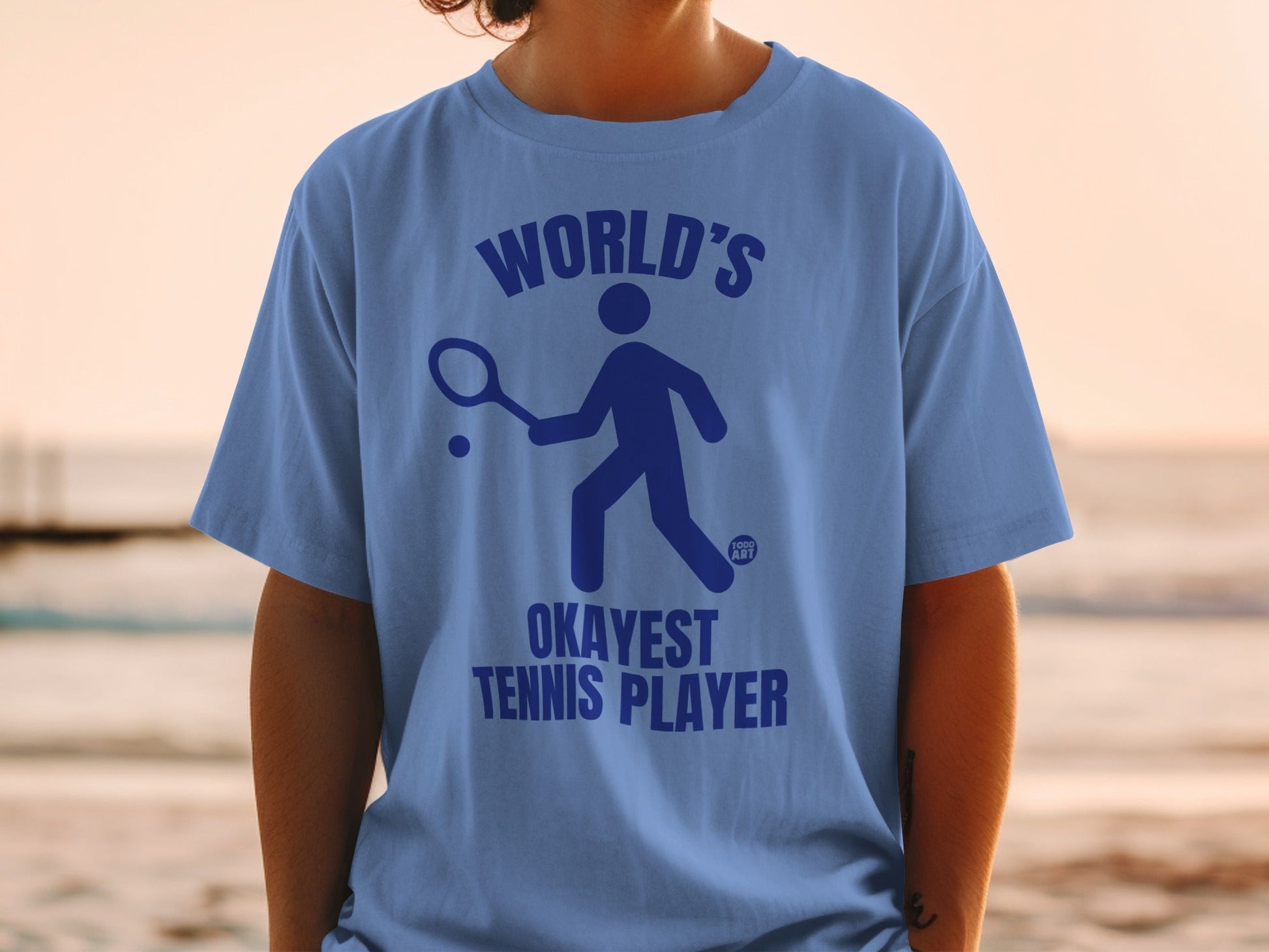 Blue t-shirt with "World's Okayest Tennis Player" graphic.