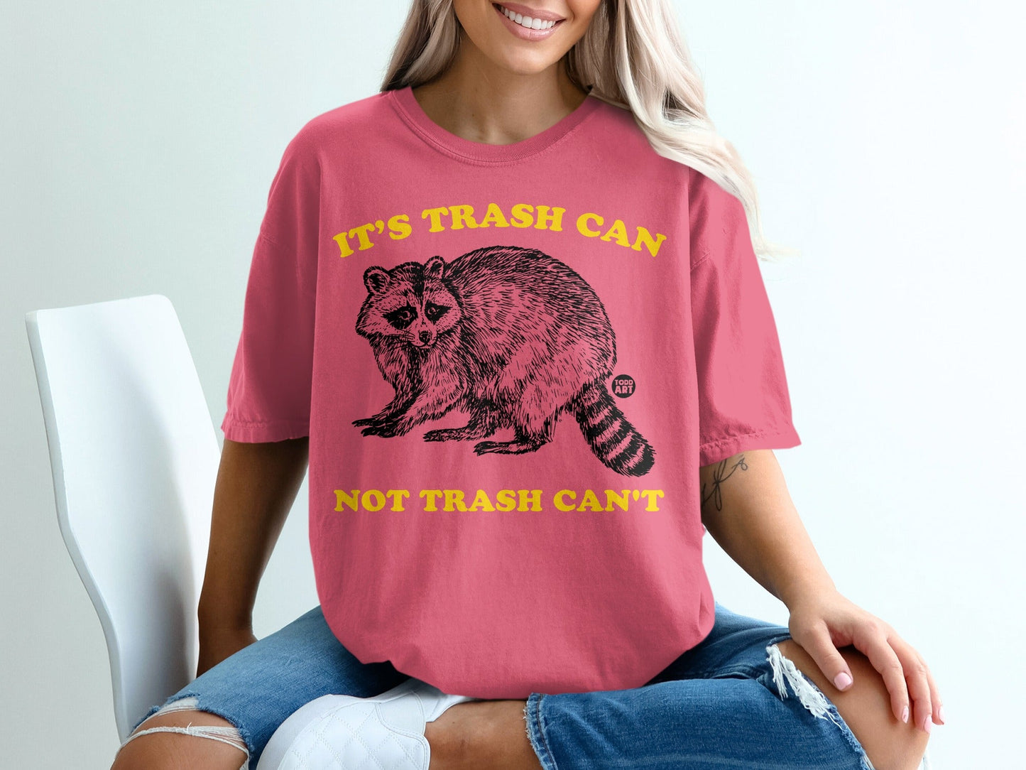 Pink t-shirt with raccoon graphic and text "It's trash can not trash can't".