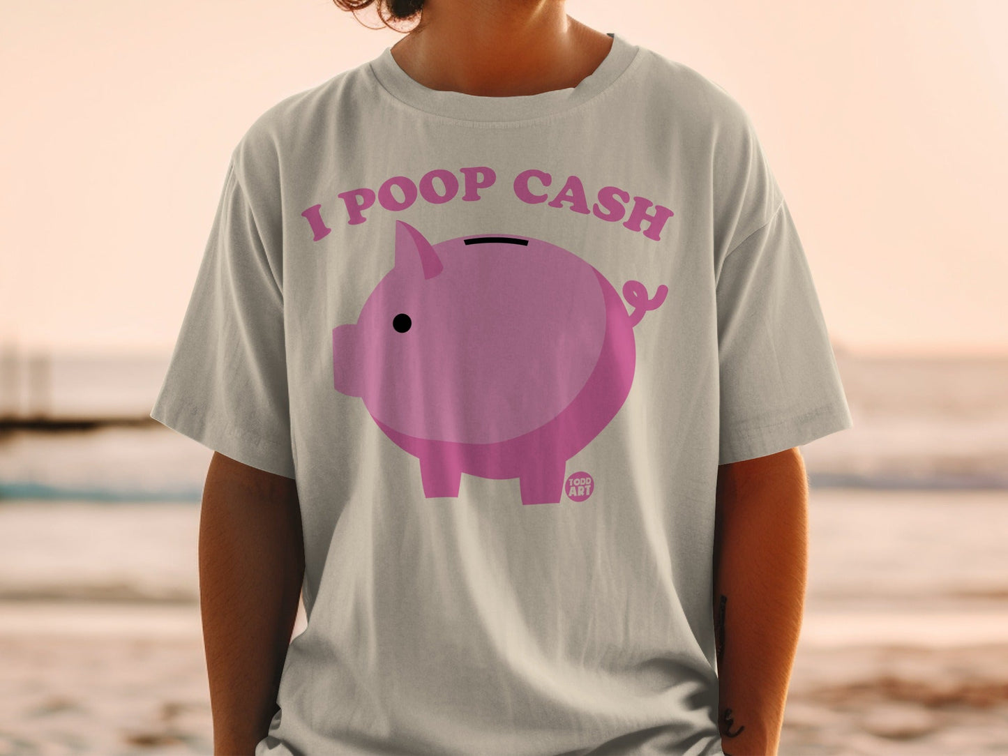 Pink piggy bank graphic with text "I POOP CASH" on a light gray t-shirt.