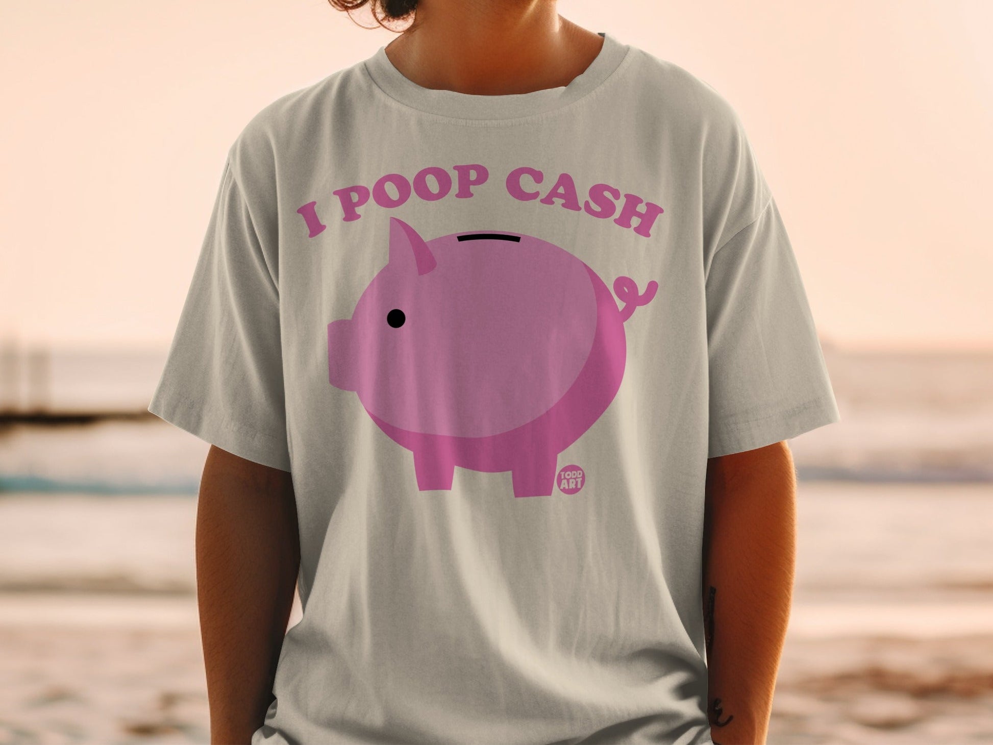 Pink piggy bank graphic with text "I POOP CASH" on a light gray t-shirt.