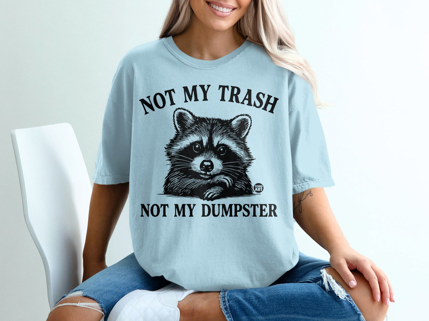 Light blue t-shirt with raccoon graphic and text "NOT MY TRASH NOT MY DUMPSTER".