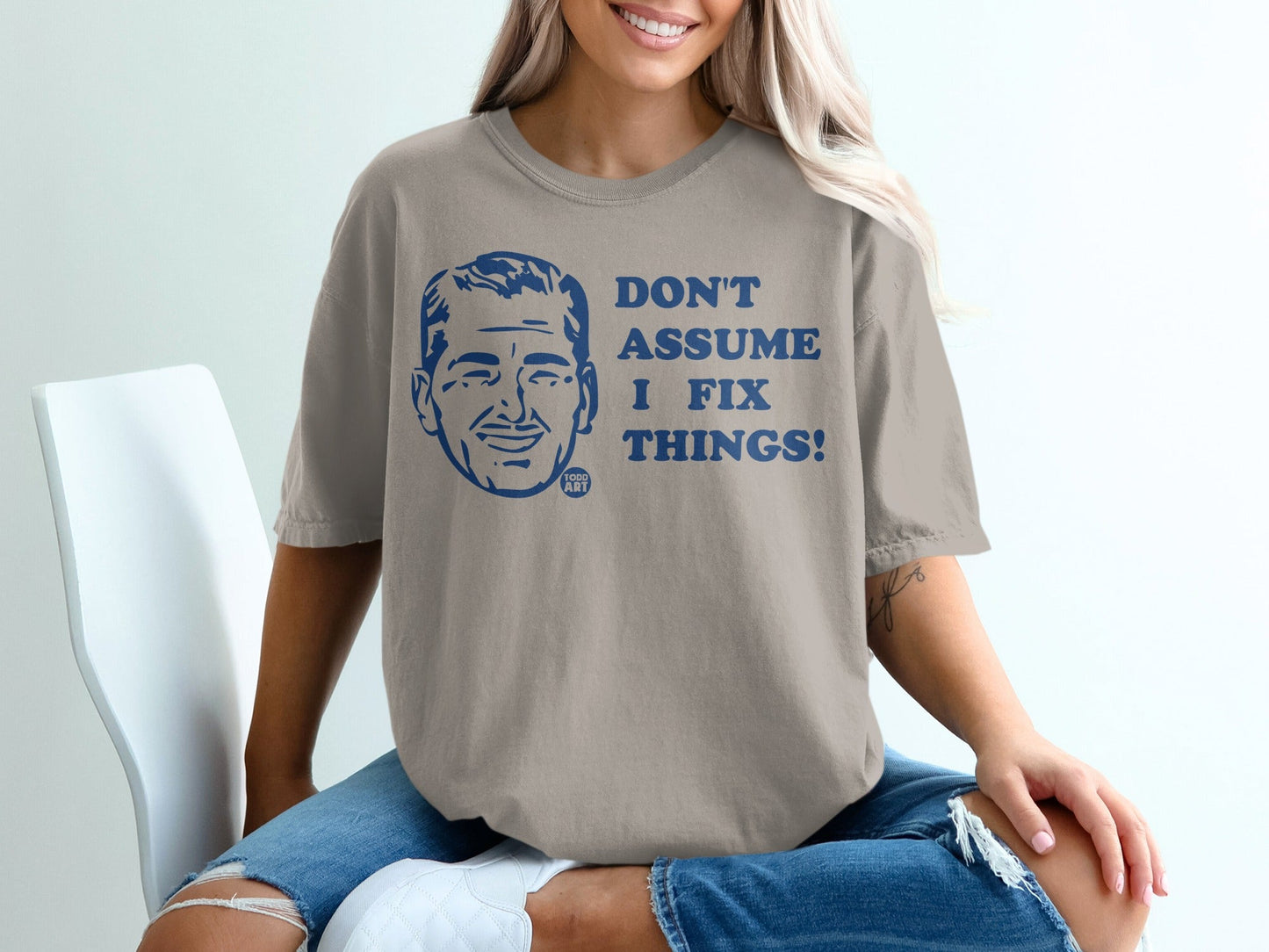 Tan t-shirt with blue graphic of a man's face and "DON'T ASSUME I FIX THINGS!"