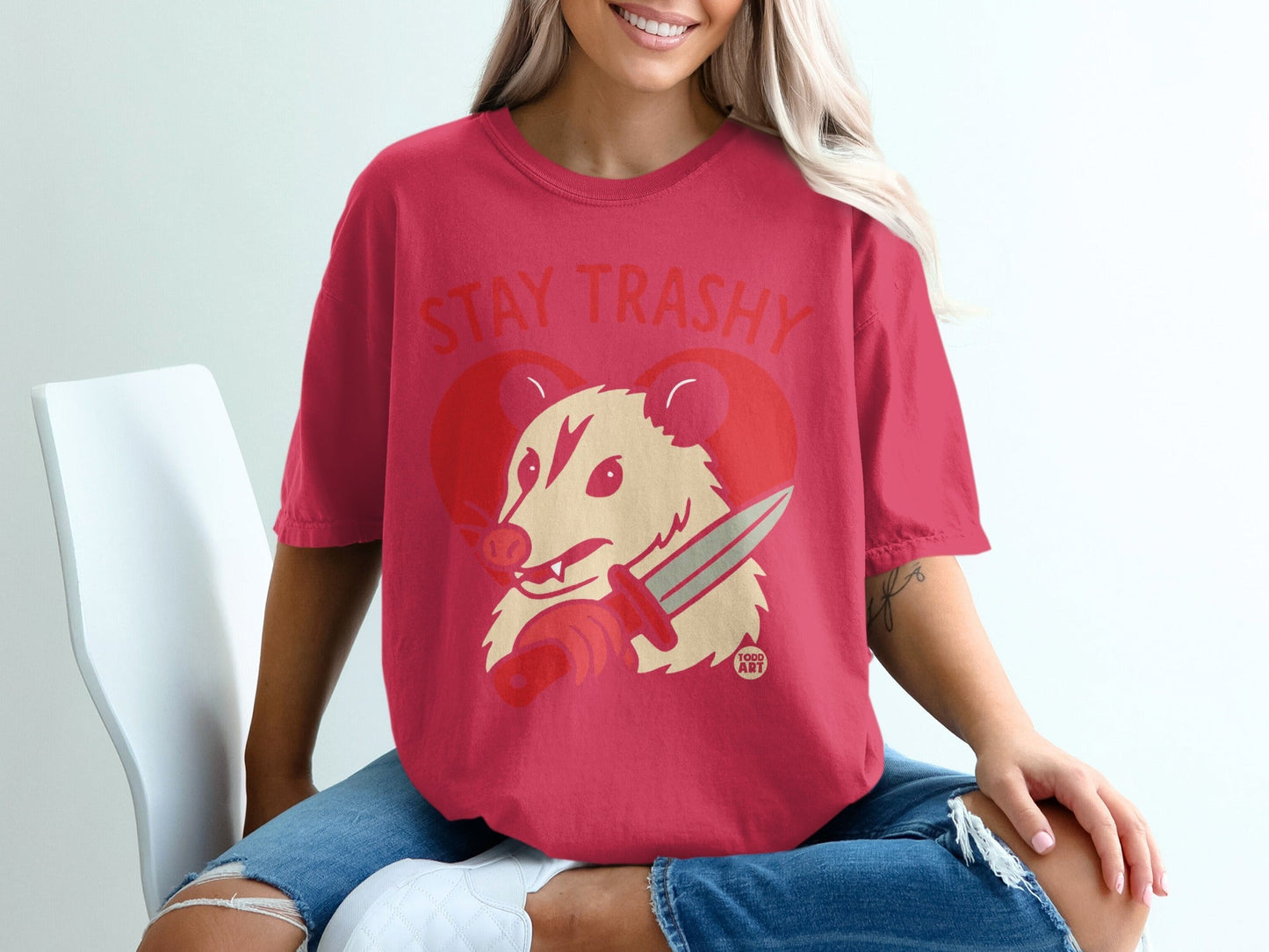 Woman wearing a pink t-shirt with a stylized possum holding a knife and the text "STAY TRASHY".