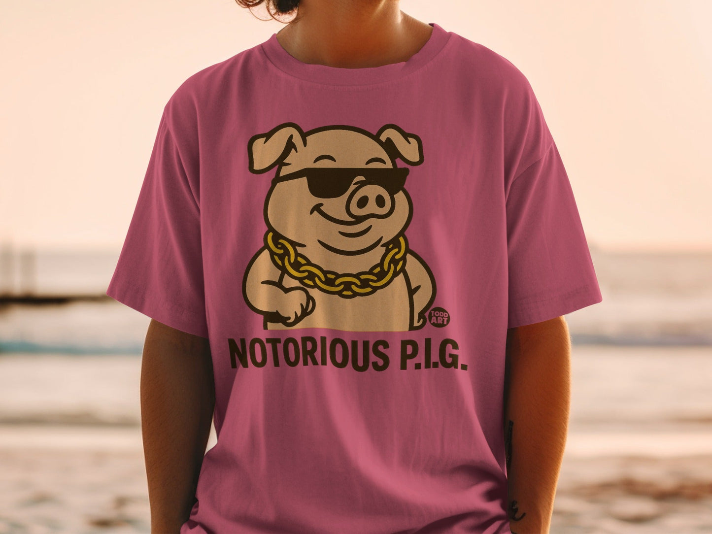 Pink t-shirt with cartoon pig wearing sunglasses and gold chain, text "NOTORIOUS P.I.G."